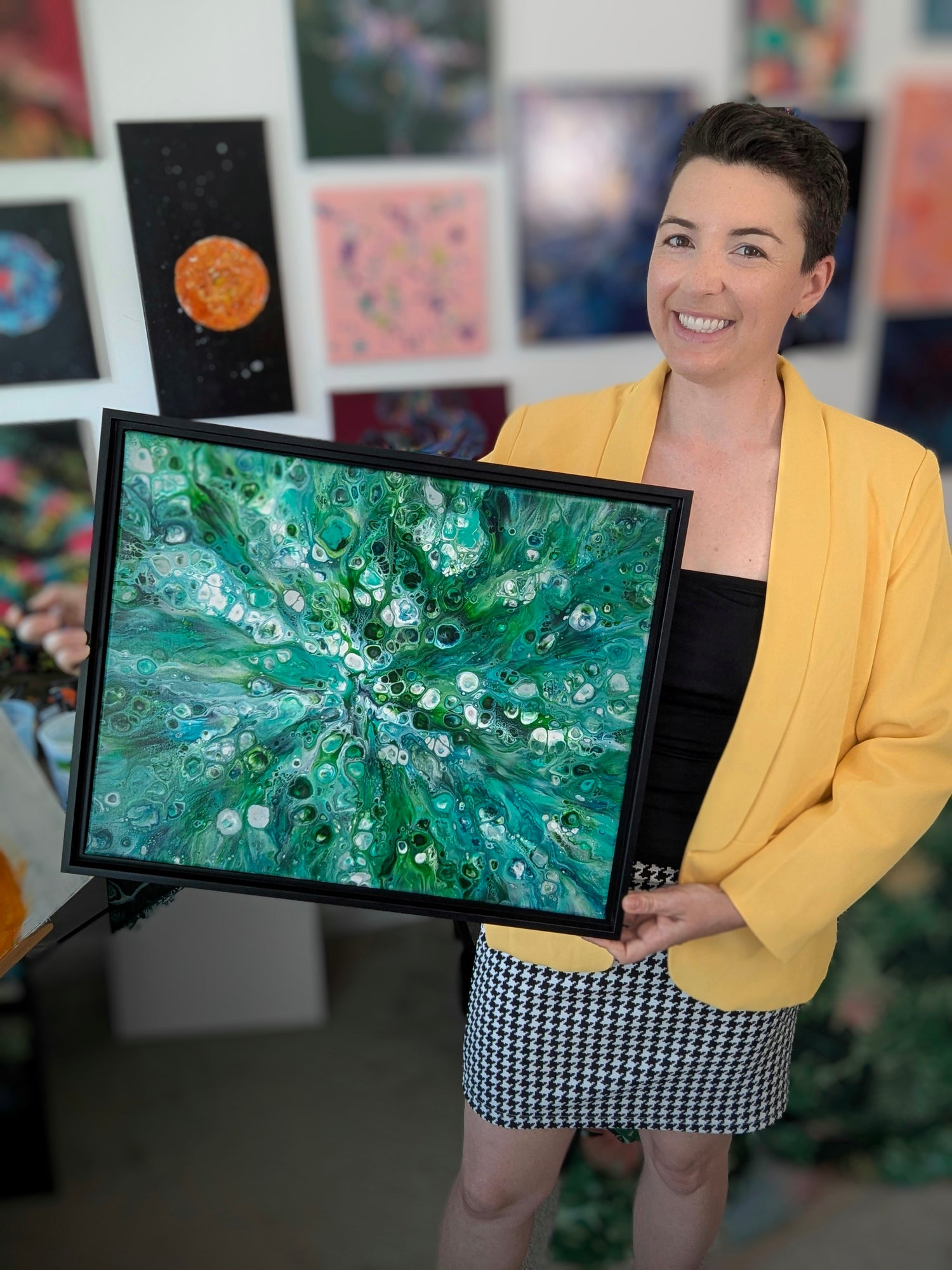 Artist Abby May with her painting Sea Maiden in her studio with artwork hanging behind her