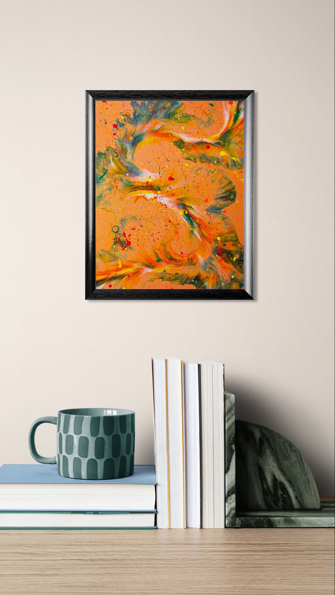 'Are You Really Going Out in That?' painting in a black frame on a beige wall, styled above a stack of books and a dark green patterned mug in a cozy reading nook.