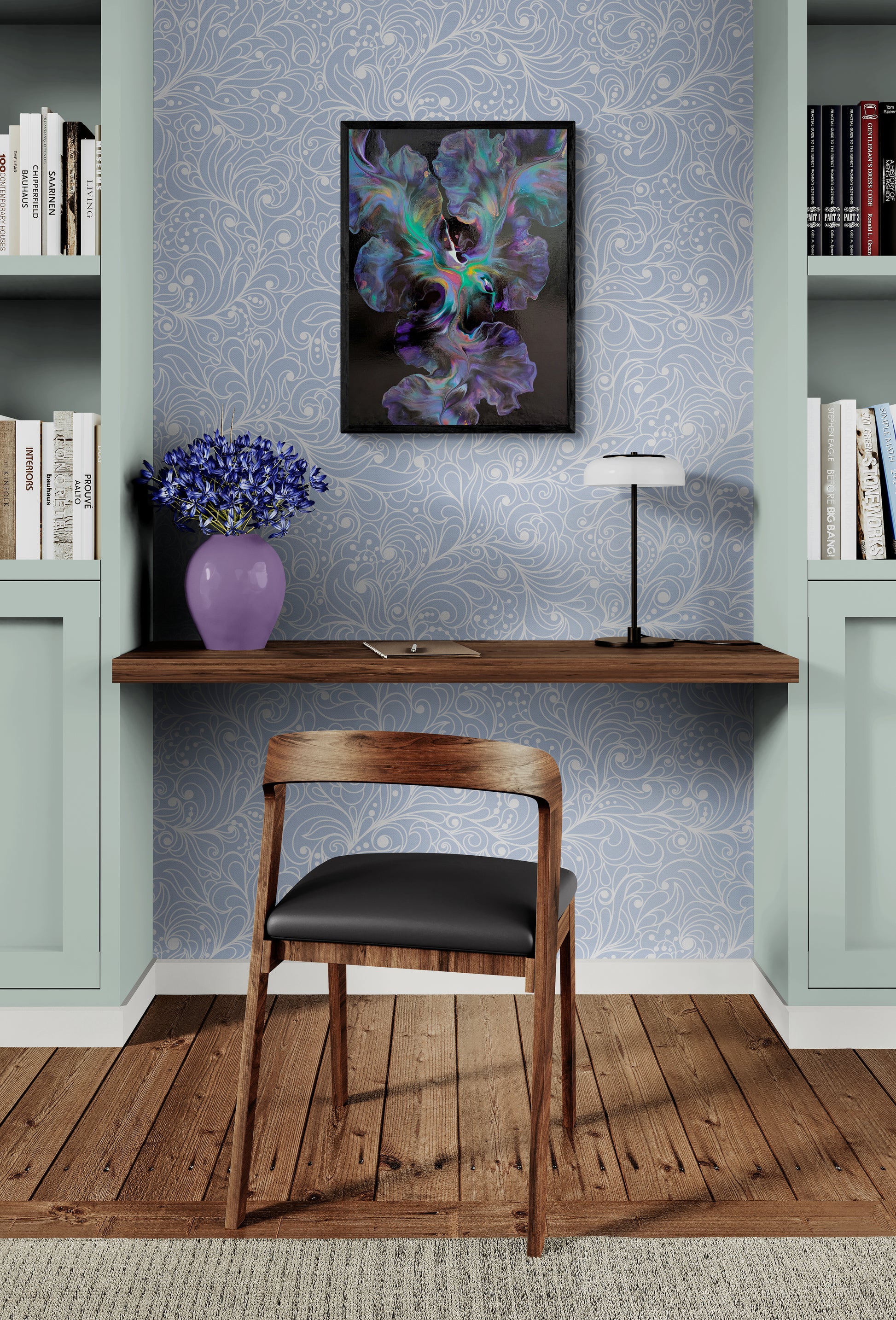 An abstract painting titled "Celestial Dance" is framed in black and displayed on a pale lavender floral wallpaper wall in a cozy built-in desk nook. The artwork features swirling blues, purples, teals, and soft auroras on a deep black background. Below, a dark wood floating desk holds a lavender vase with purple flowers, a black and white lamp, and a notebook, with a modern wood and leather chair placed on warm wooden floors.