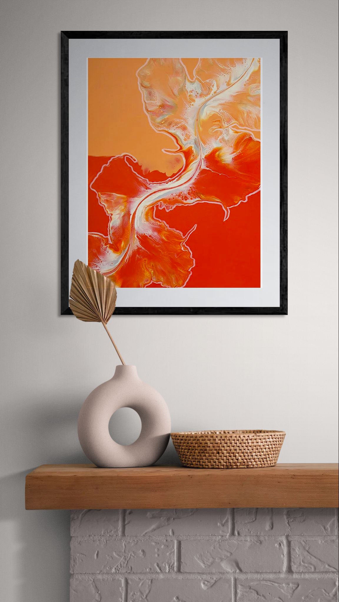 Acrylic fluid art print Cross the Line in bold fiery red and orange hues, framed with a white mat, displayed above a wooden mantle styled with a sculptural vase and woven basket.
