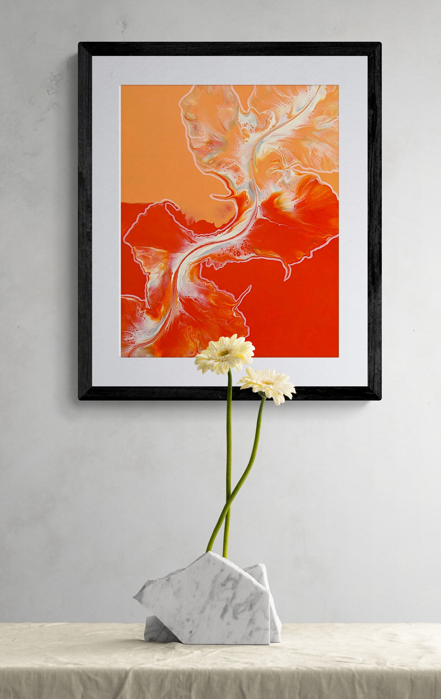 Framed acrylic fluid art print titled Cross the Line, in bold red and orange with flowing white and golden accents, displayed on a gray wall above a marble vase with white daisies.
