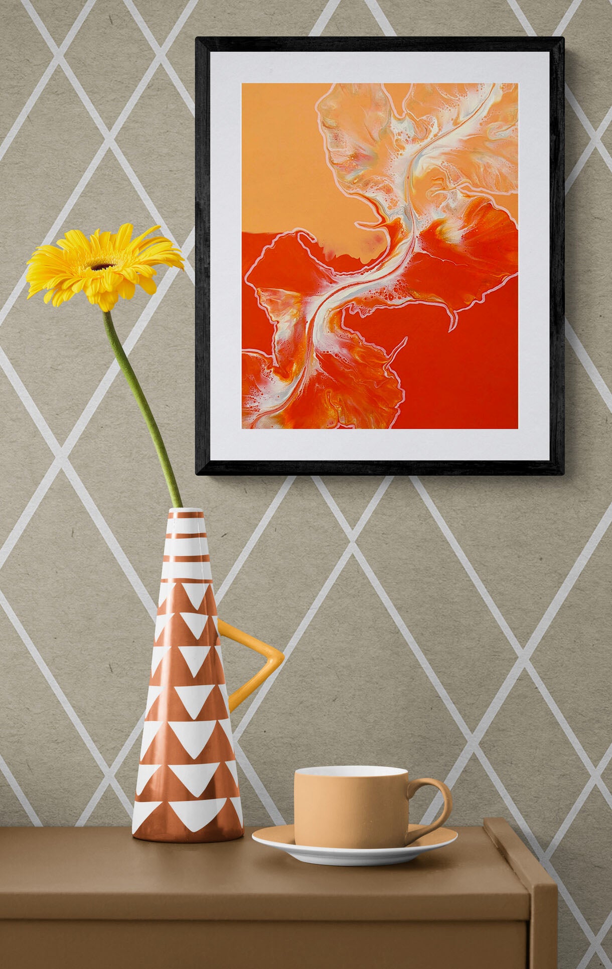 Framed acrylic fluid art print Cross the Line with dynamic red and orange tones accented by white and gold, hung on a patterned wall above a console table with a bold orange vase holding a yellow flower.