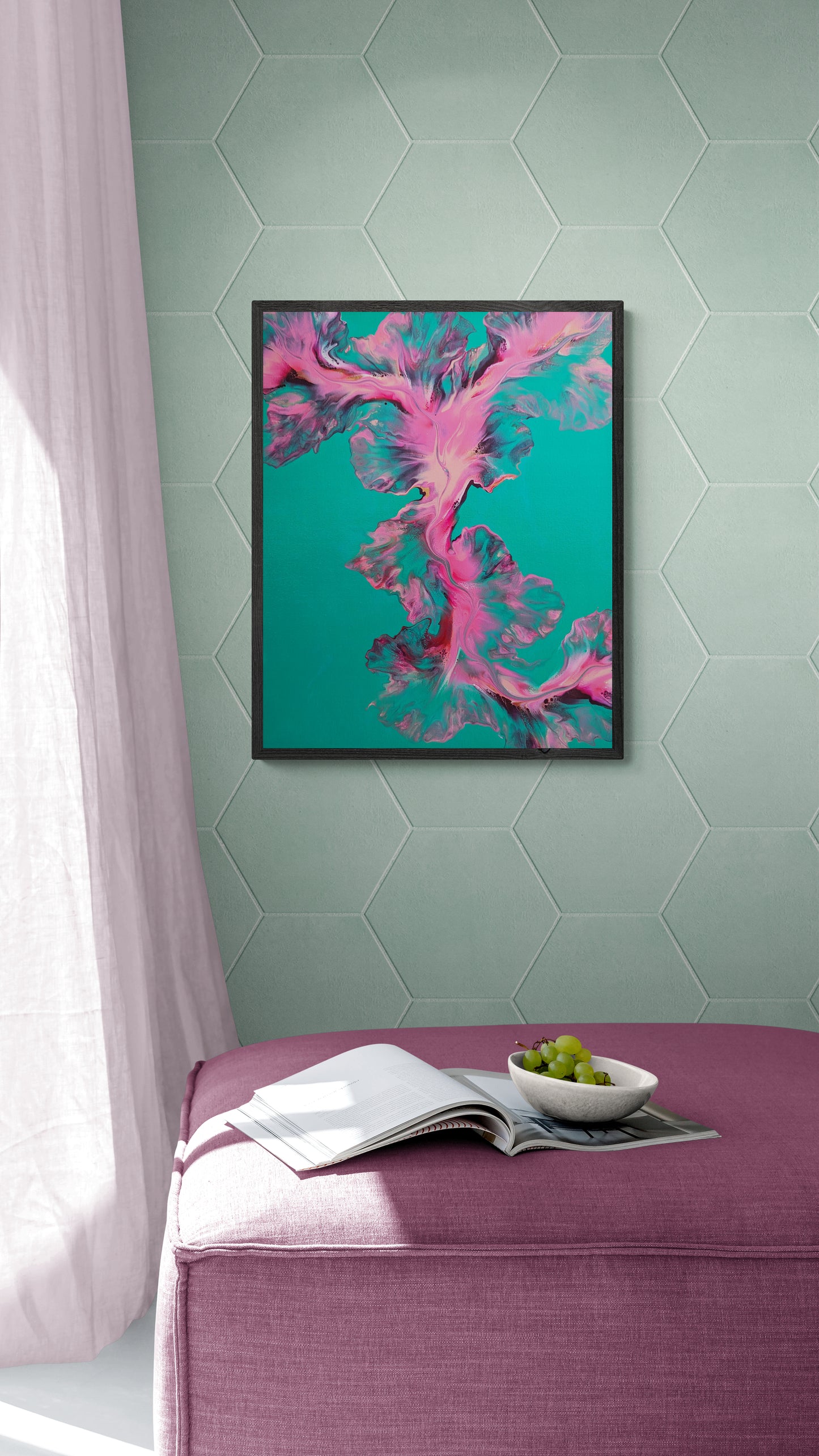 Framed abstract fluid painting with swirling pink, blue, and neon hues on a vibrant turquoise background, hanging on a pale hexagon-tiled wall above a mauve ottoman with a bowl of grapes and an open book.