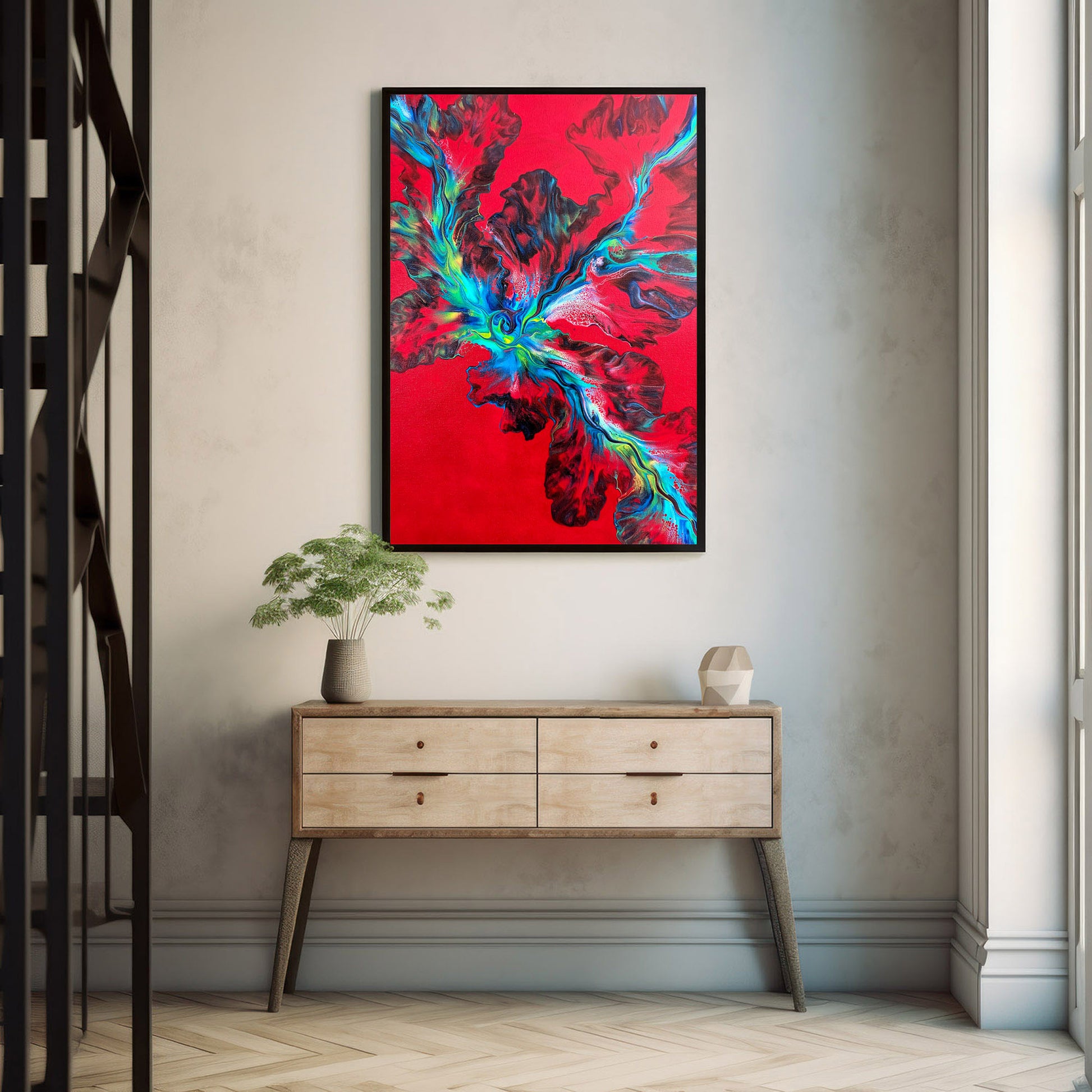The painting "Elemental Surge" hangs centered above a light wood console table in a bright, minimalist hallway. The vivid red background and explosive teal and black forms of the artwork pop against the soft gray walls, lit by natural daylight.
