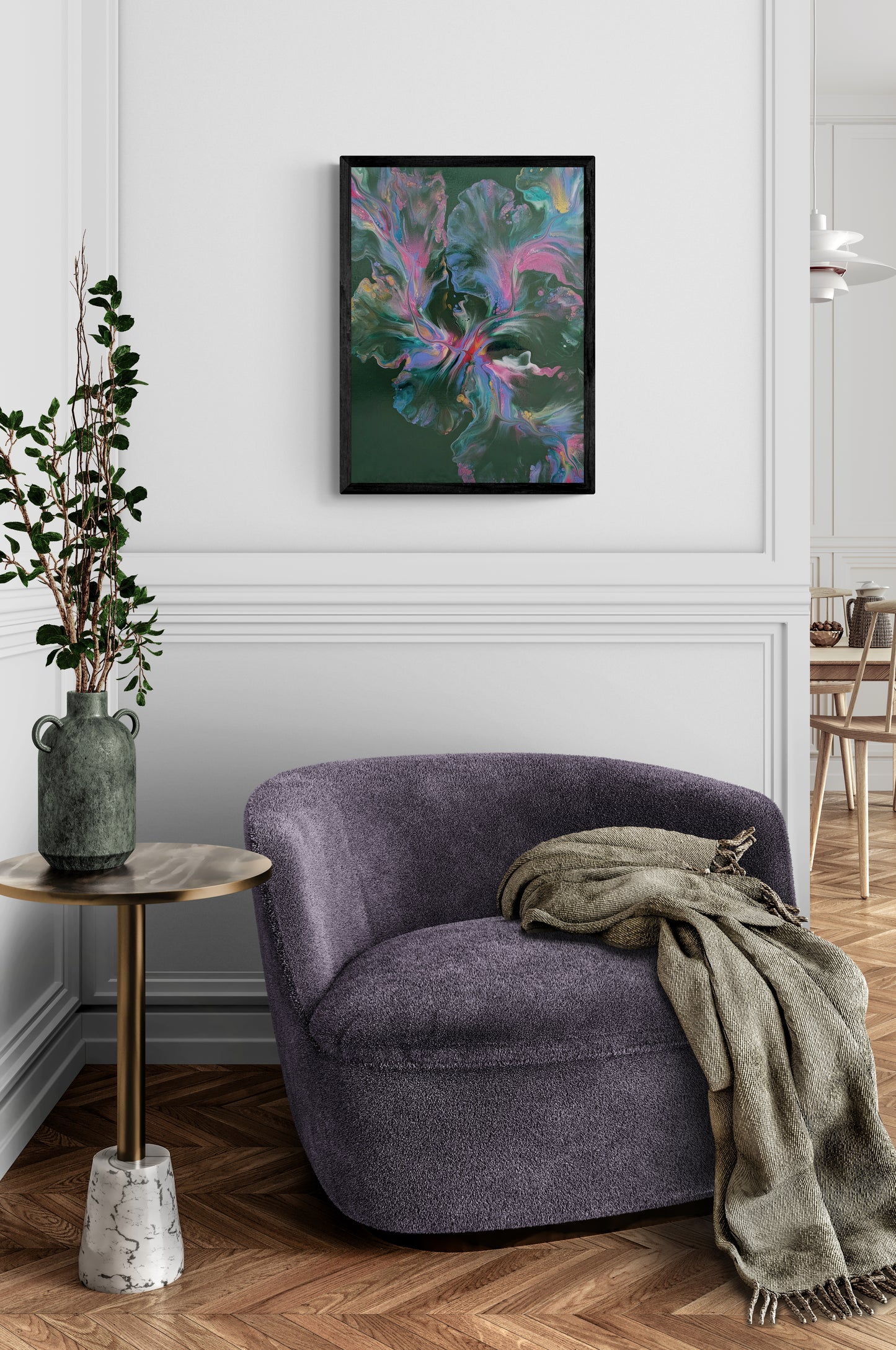 An abstract painting titled "Enchanted Sky" is framed in black and mounted on a white-paneled wall above a soft lavender boucle chair. The artwork features dreamy swirls of pink, teal, gold, and lavender over a deep forest green background. The cozy corner includes a stone and wood side table topped with a green ceramic vase of greenery, and a soft olive throw draped across the chair, creating a calming, elevated reading nook with artistic charm.