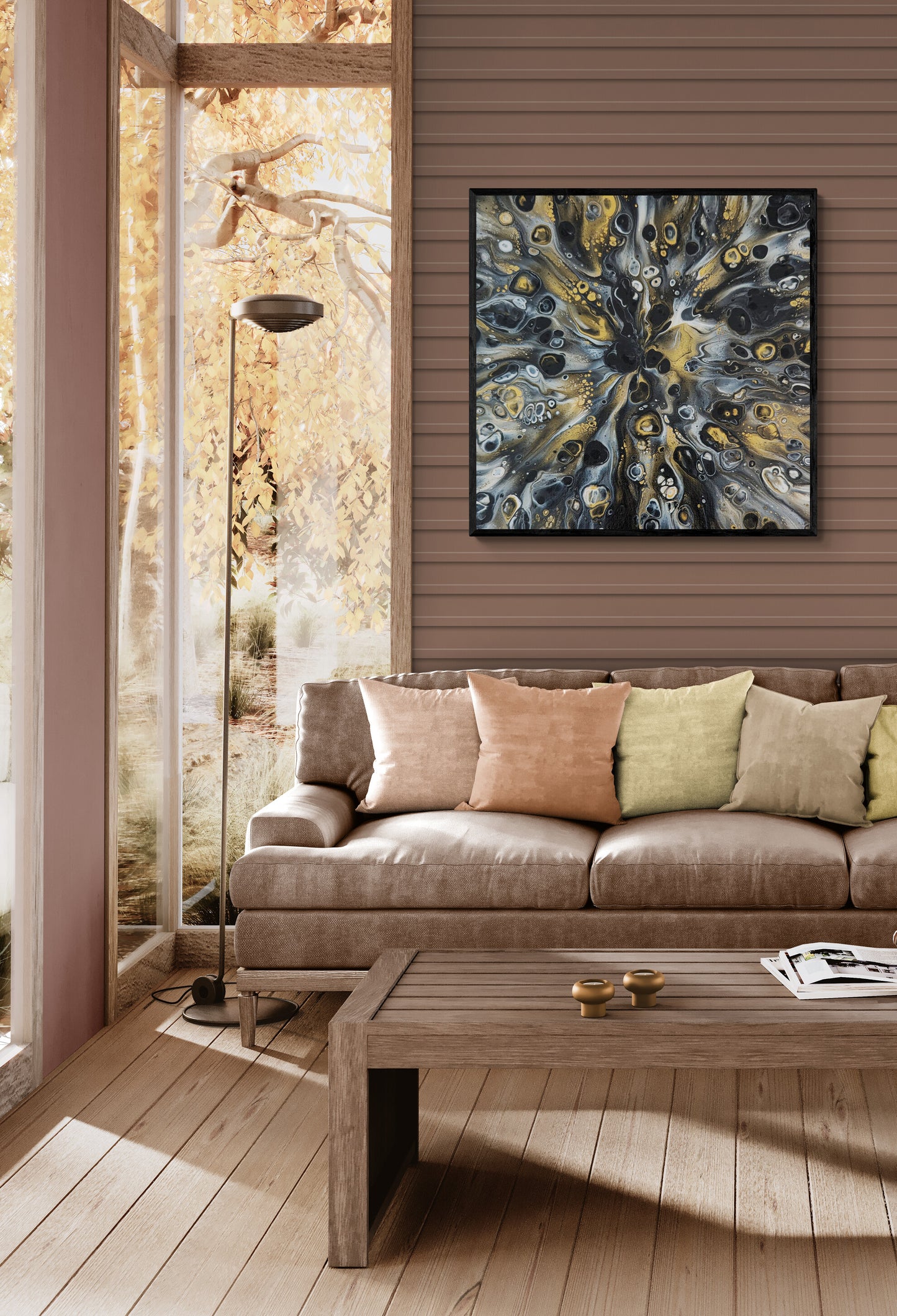 A square abstract painting titled “Glamorous” hangs above a tan sofa with pastel pillows in a cozy living room. The artwork features metallic gold, black, white tones radiating outward, creating a sense of depth and movement against the warm wood-paneled wall.