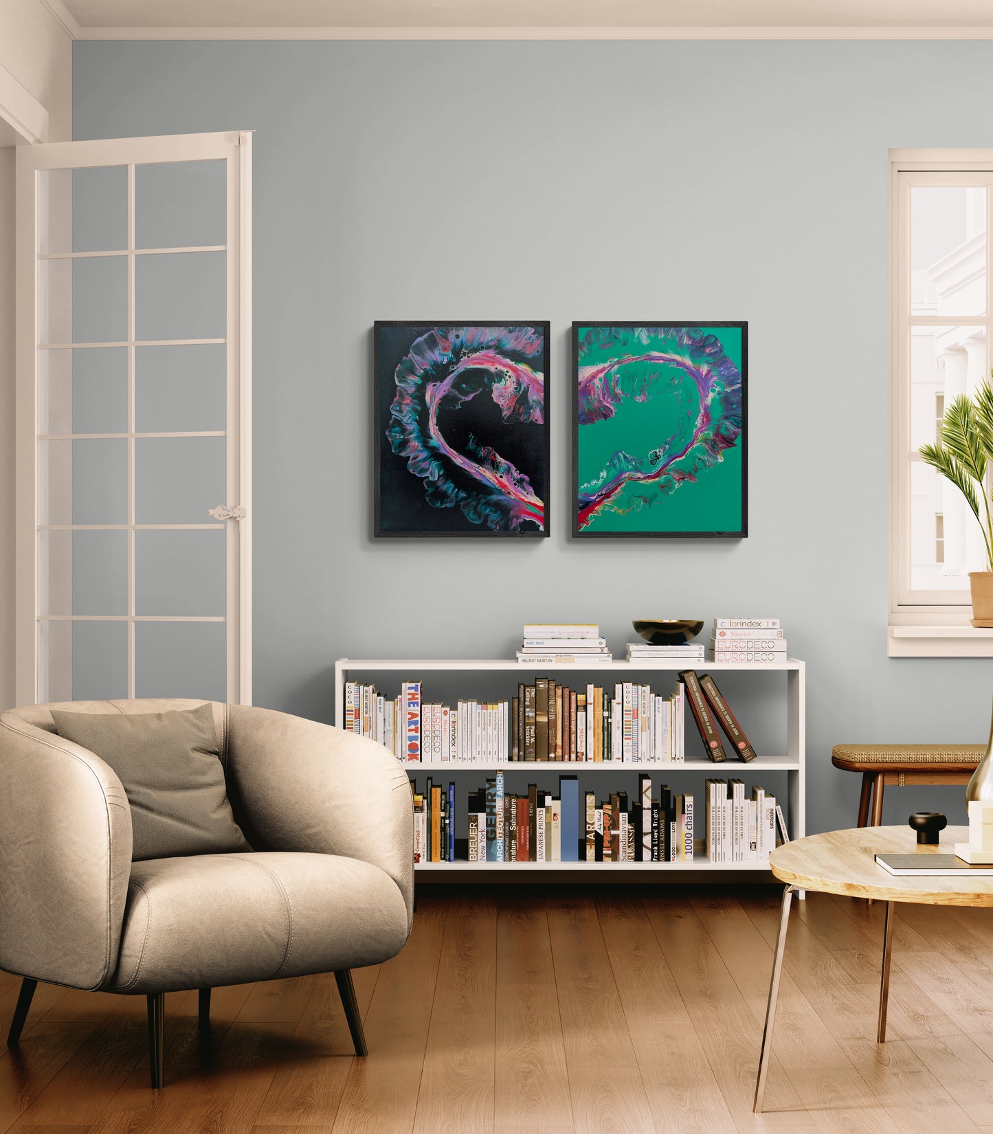 Two abstract heart-shaped fluid paintings are displayed side by side above a white bookcase in a modern living room. One canvas has a black background with vivid pink, teal, and purple accents. The other features a green background with matching flowing colors. Together, the canvases form a single heart shape, creating a bold, emotional centerpiece in the softly lit space.