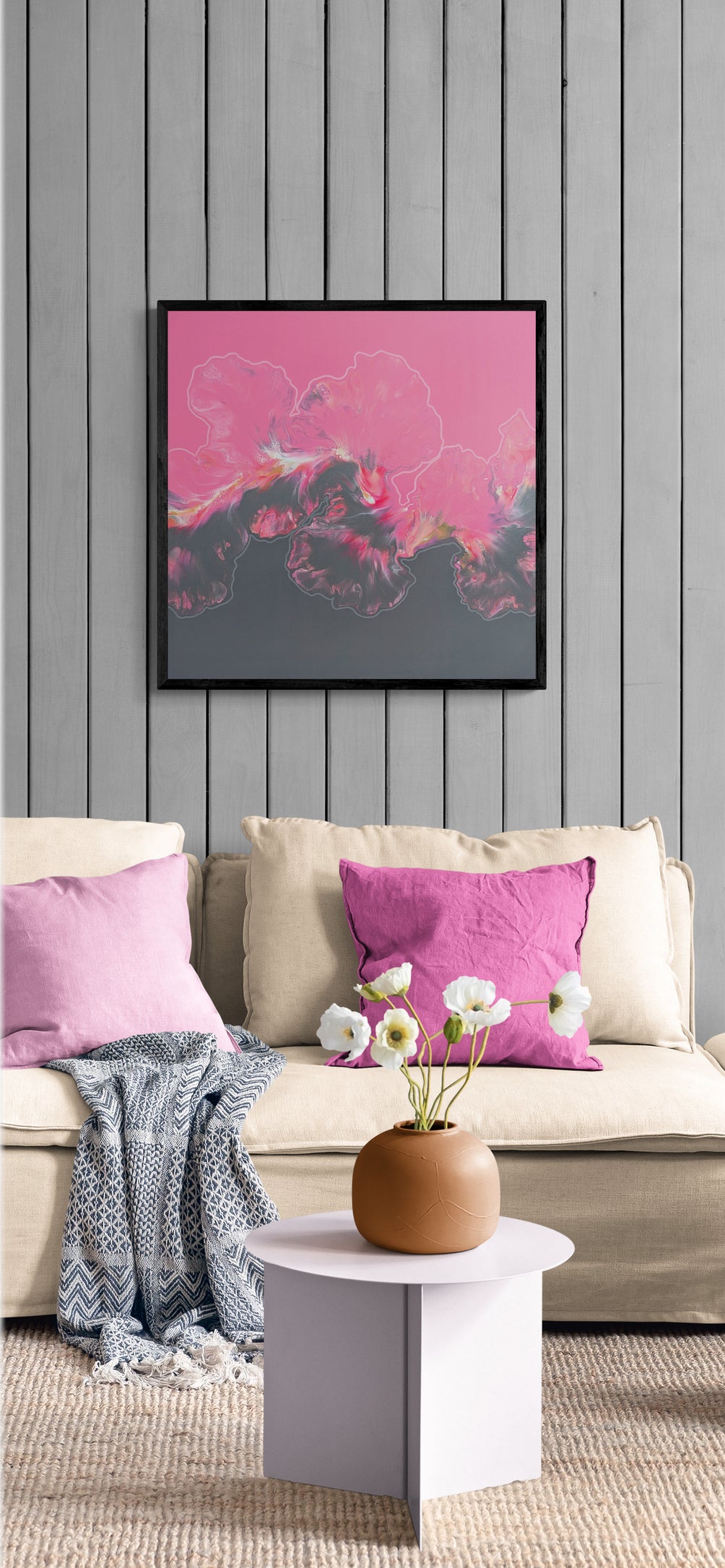 Abstract painting titled “In My Bliss” with pink and charcoal tones, displayed above a beige couch with pink pillows and a small flower arrangement on a pale coffee table.