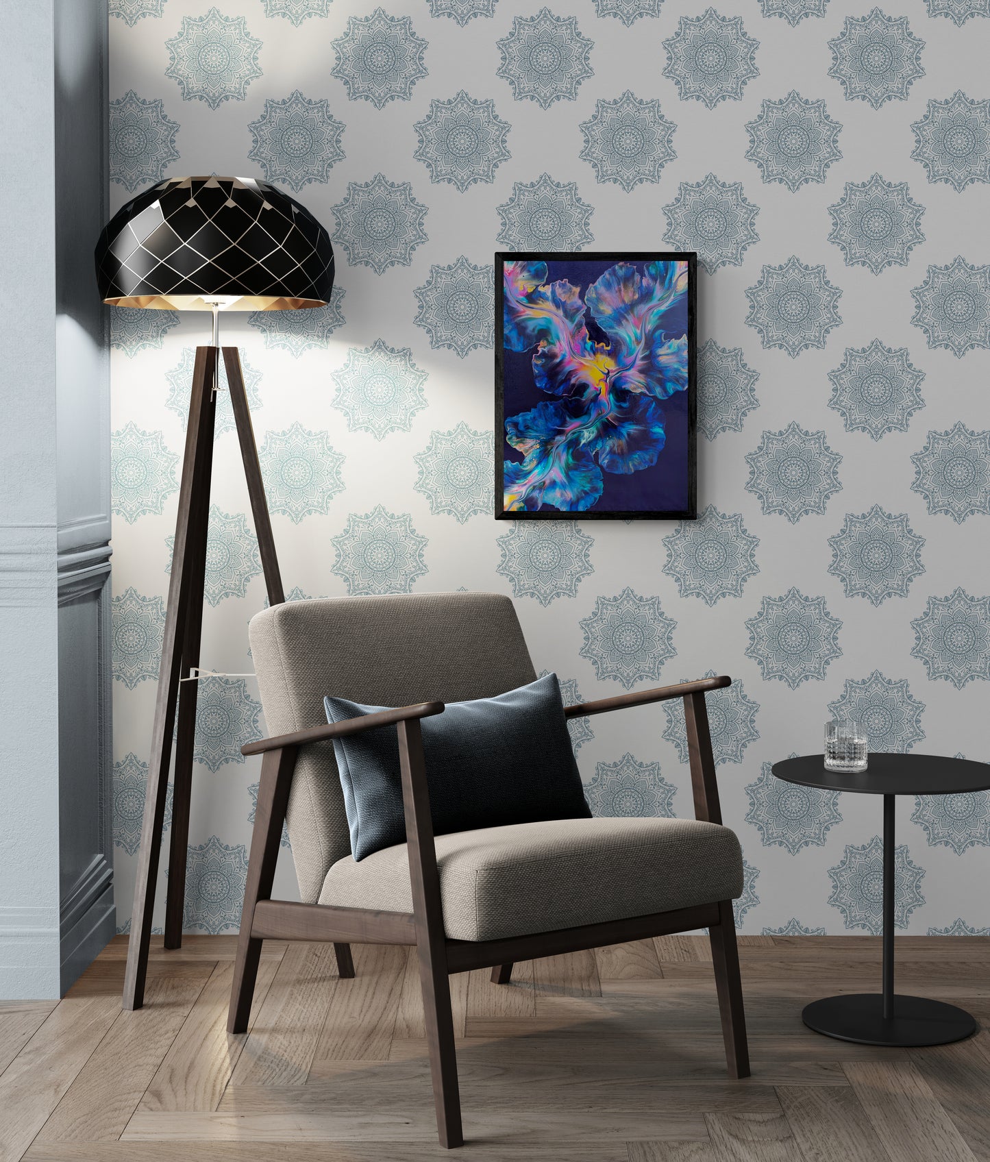 An abstract painting titled "Nebula Bloom" is framed in black and displayed on a white wall with intricate blue mandala patterns. The artwork features radiant swirls of teal, cobalt, violet, and golden yellow over a deep navy background. Below, a modern cream armchair with a navy pillow sits beside a small round black table and a tall tripod lamp, creating a serene and stylish reading nook with celestial energy.