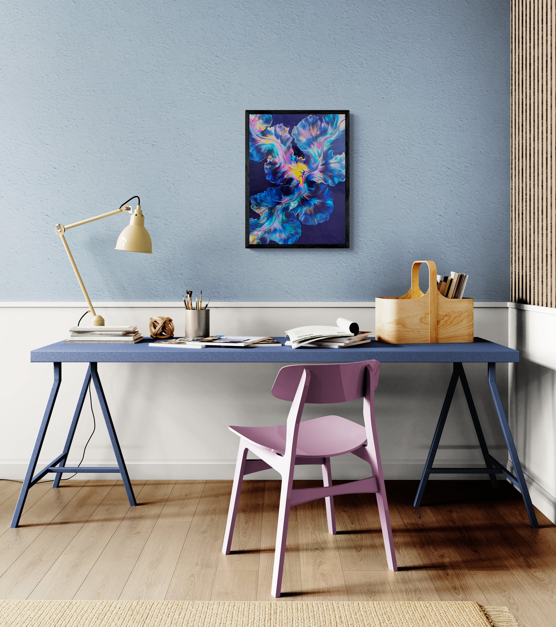 An abstract painting titled "Nebula Bloom" is framed in black and displayed on a blue wall above a deep periwinkle desk. The artwork features vibrant cosmic swirls of blue, teal, pink, purple, and yellow over a navy background. The creative space includes a lavender chair, cream desk lamp, books, and a wooden organizer, creating a modern and playful workspace with a spark of galactic wonder.