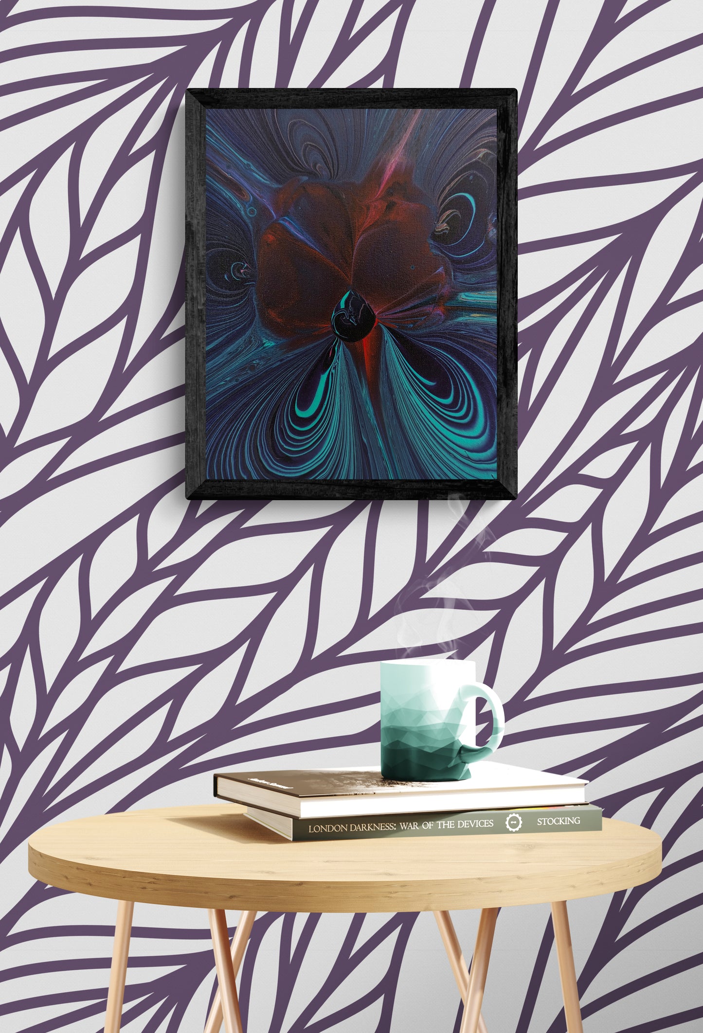 Framed abstract fluid painting with deep black, red, teal, and violet tones displayed on a bold violet-leaf patterned wallpaper, above a round wood table with a steaming green mug and stacked books.