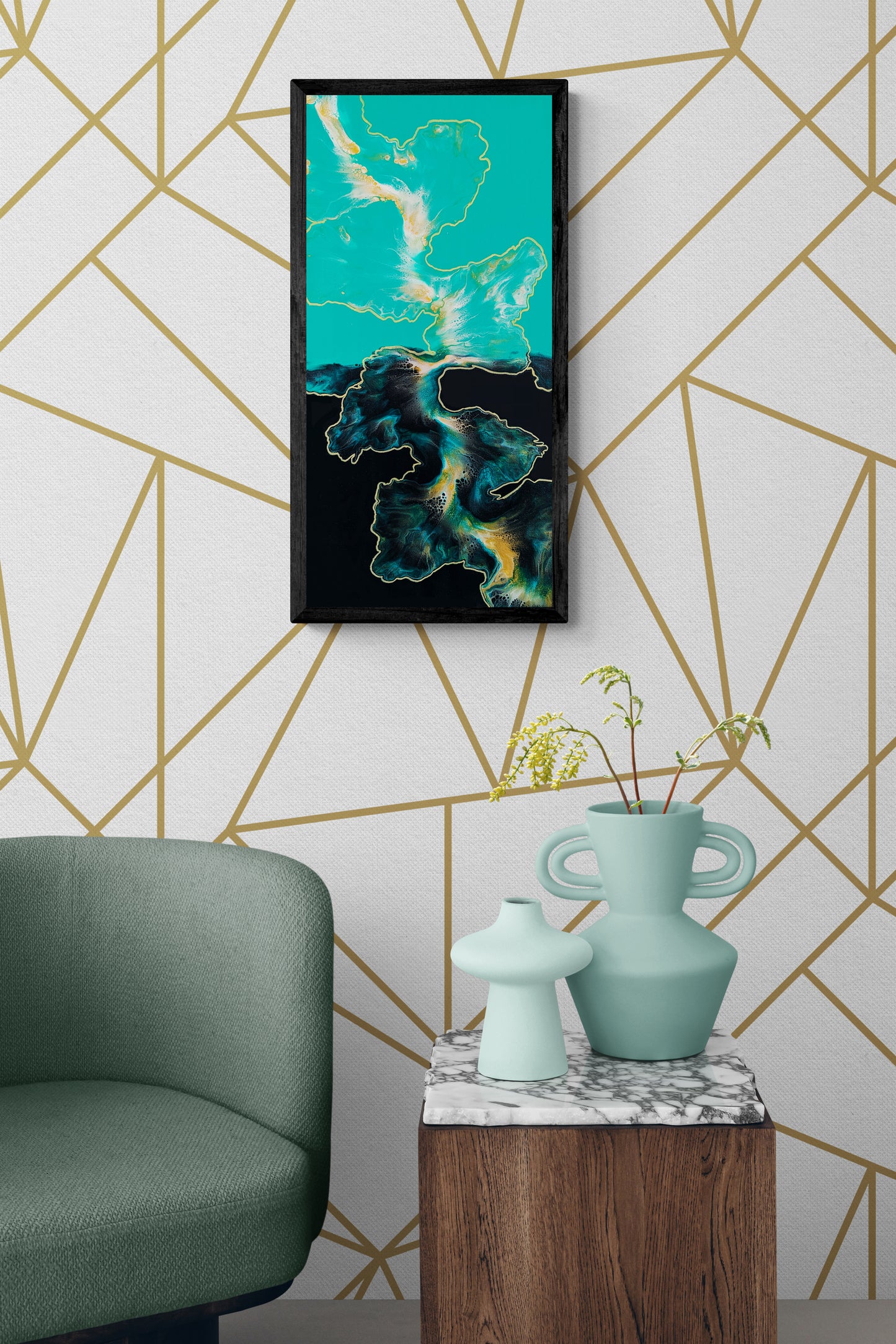 A bold abstract painting titled "Outside the Lines" is framed in black and displayed on a white wall with a geometric gold line pattern. The painting features fluid shapes in teal, gold, white, and black, resembling topographical land and sea. A sage green armchair sits beside a marble-topped wooden side table, which is styled with sculptural mint-green vases and a sprig of greenery, creating a high-style, design-forward interior.