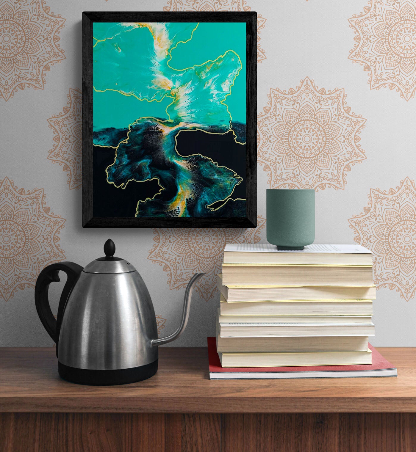 Framed teal and gold abstract painting on a wall with mandala-inspired wallpaper, styled with books and a teapot.