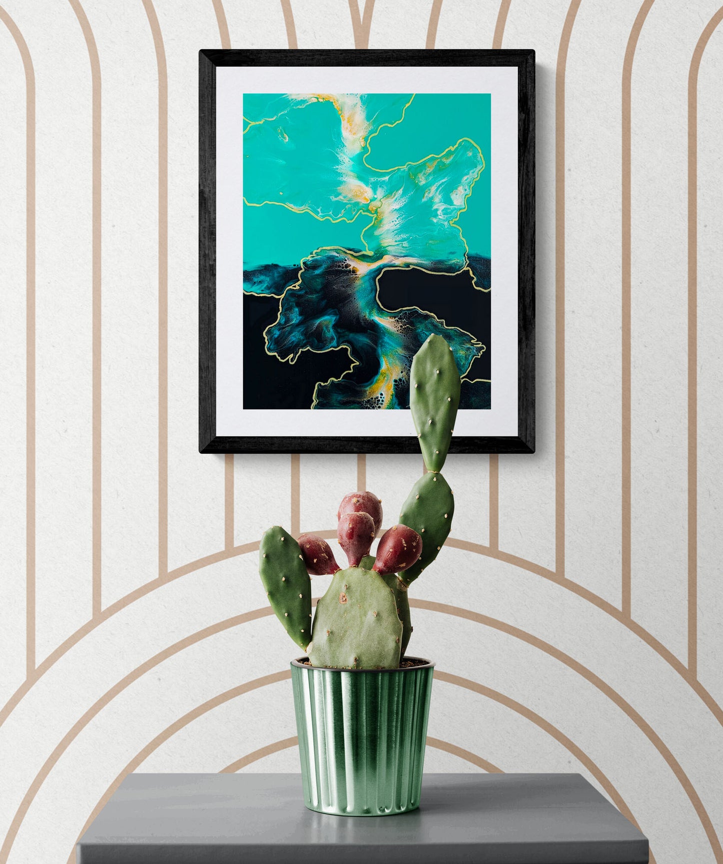 Abstract turquoise and black fluid art print with golden accents styled above a cactus plant in a minimal interior.