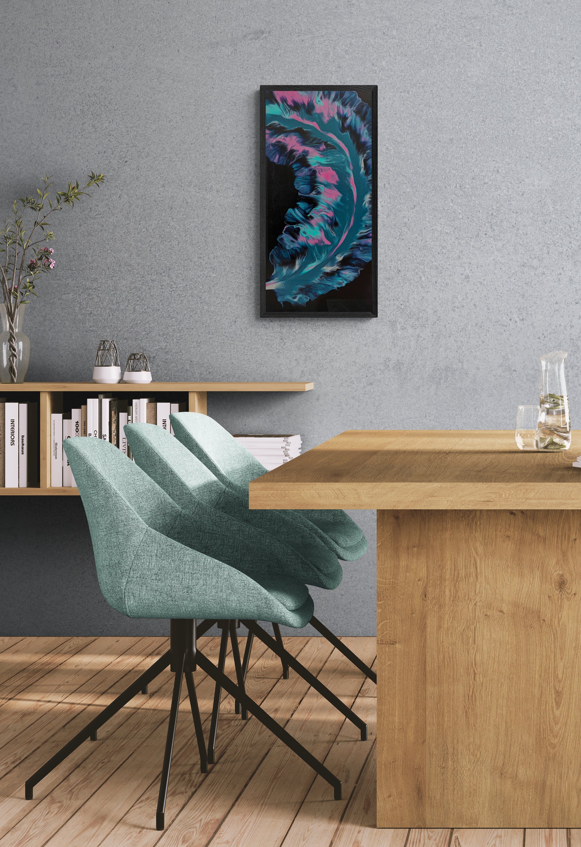 Framed abstract painting with flowing teal, pink, and violet tones on a black background, hanging on a gray textured wall above a wood dining table with mint green chairs and minimalist shelving.