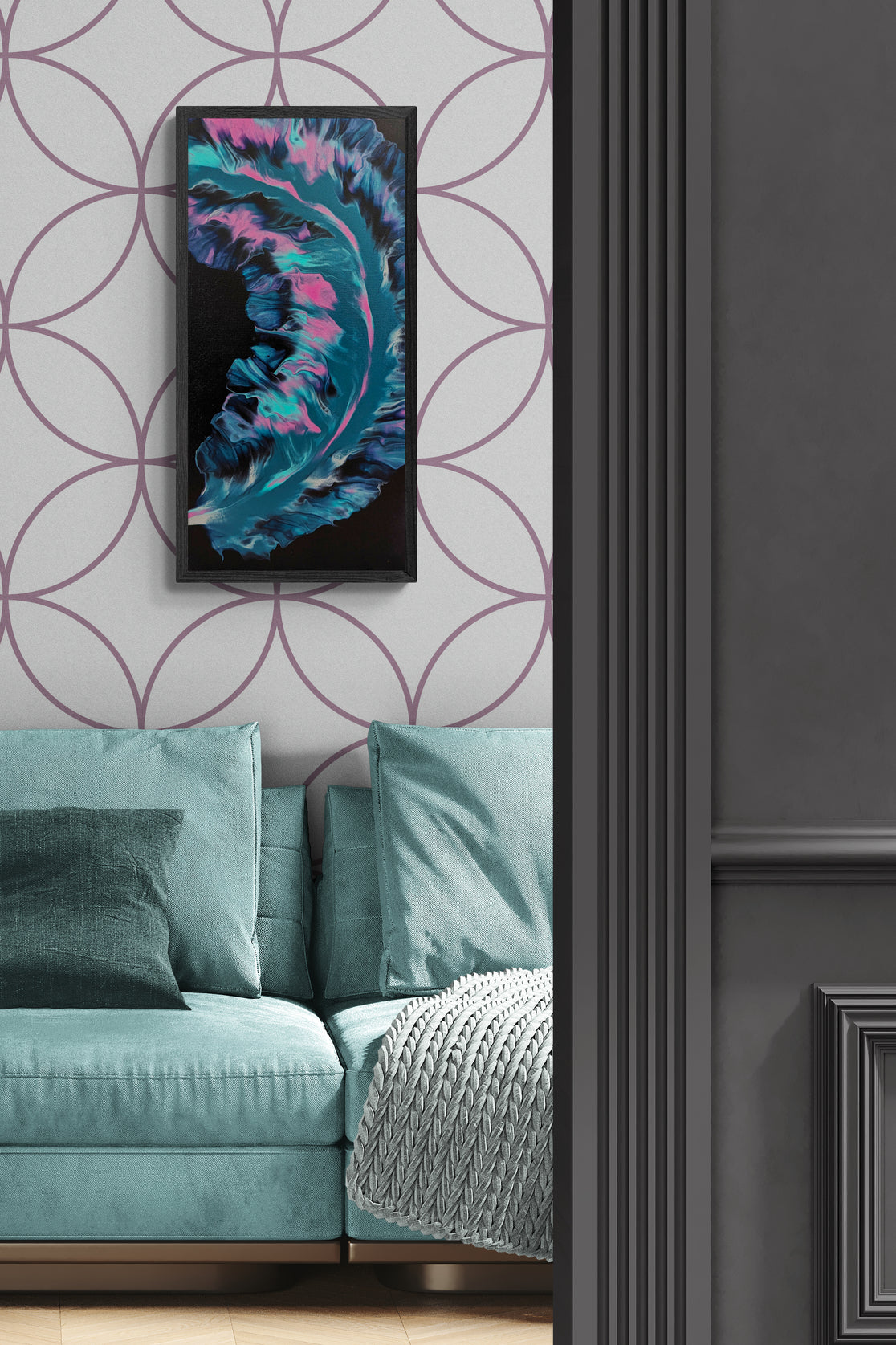 Framed abstract painting featuring glowing teal, pink, and violet forms on a black background, displayed above a teal couch with textured pillows and throw blanket, against mauve geometric wallpaper.