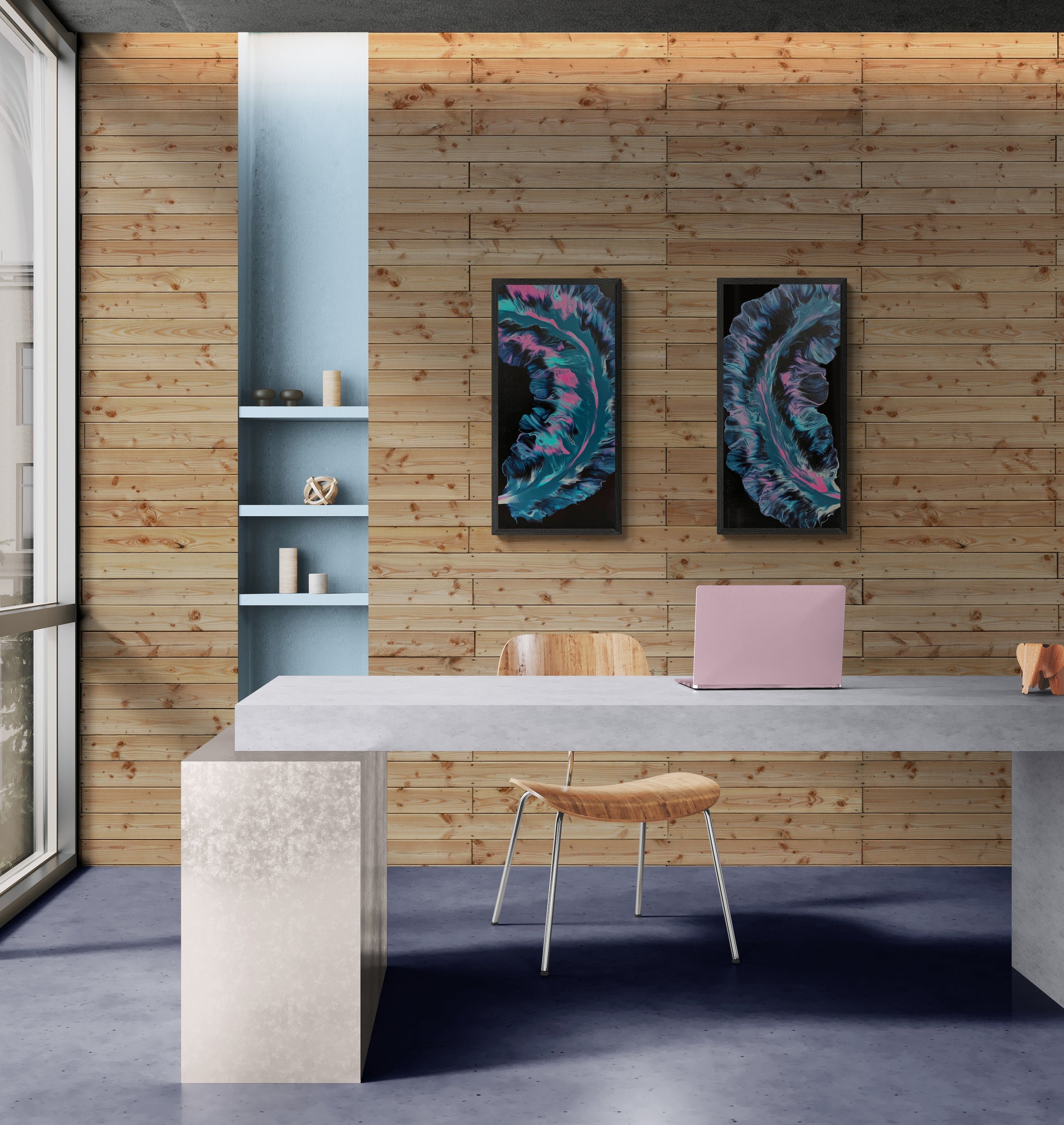 Two framed abstract paintings featuring swirling teal, pink, and violet forms on a black background, displayed side by side on a wooden wall above a minimalist concrete desk in a modern office.
