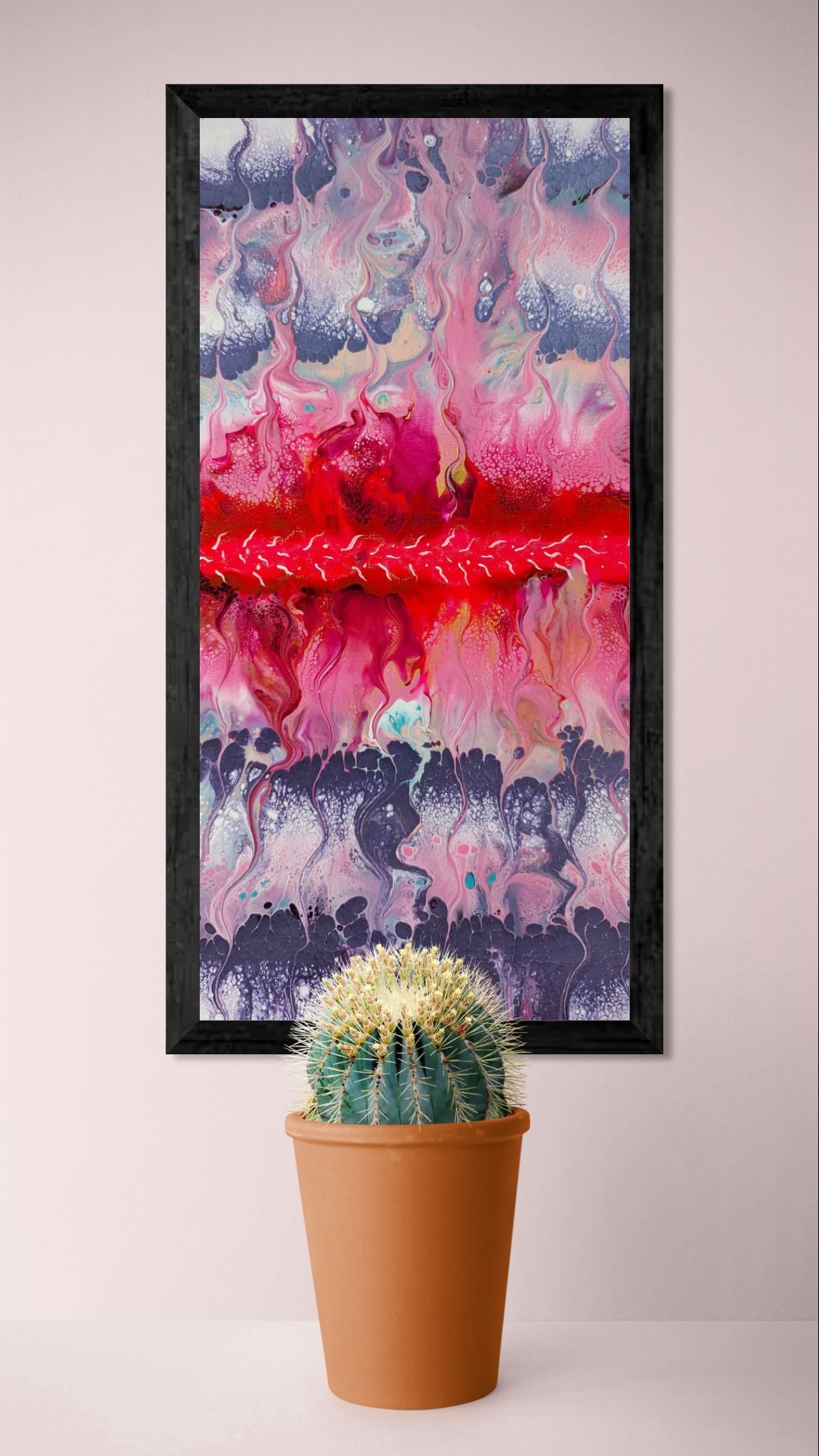 Framed vertical fluid acrylic painting in pink and purple tones displayed on a soft pink wall above a potted cactus.
