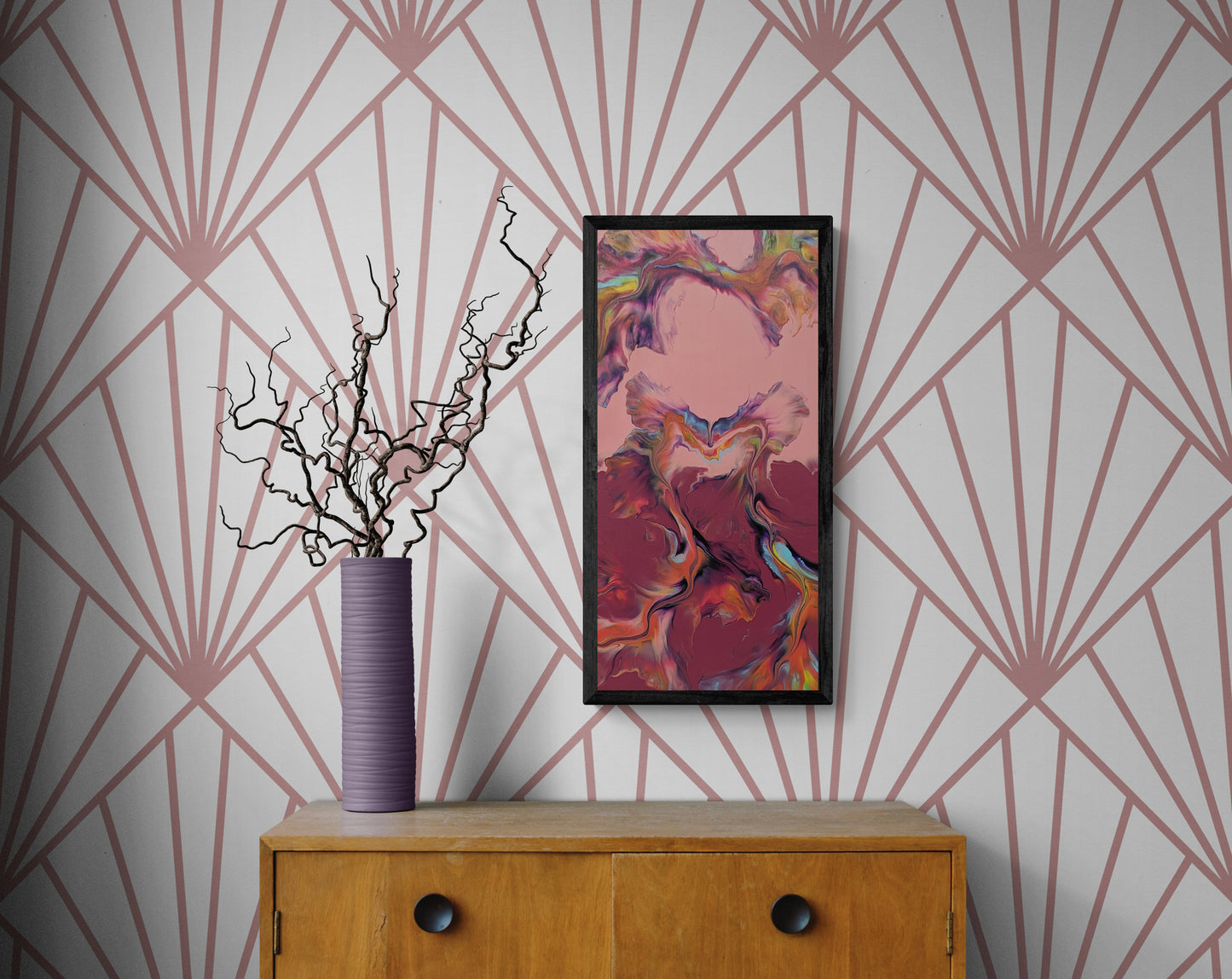 Framed abstract painting in rose, plum, and deep red tones displayed on a wall with geometric pink-and-white wallpaper, above a wooden cabinet with a tall purple vase holding curly branches.