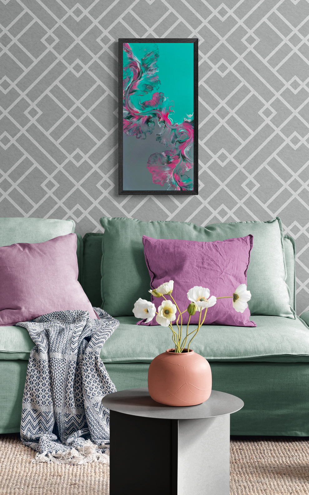 “Slow Ascent” abstract painting displayed in a soft black frame above a sage green sofa with purple pillows, patterned wallpaper, and a round table with a pink vase and white flowers.