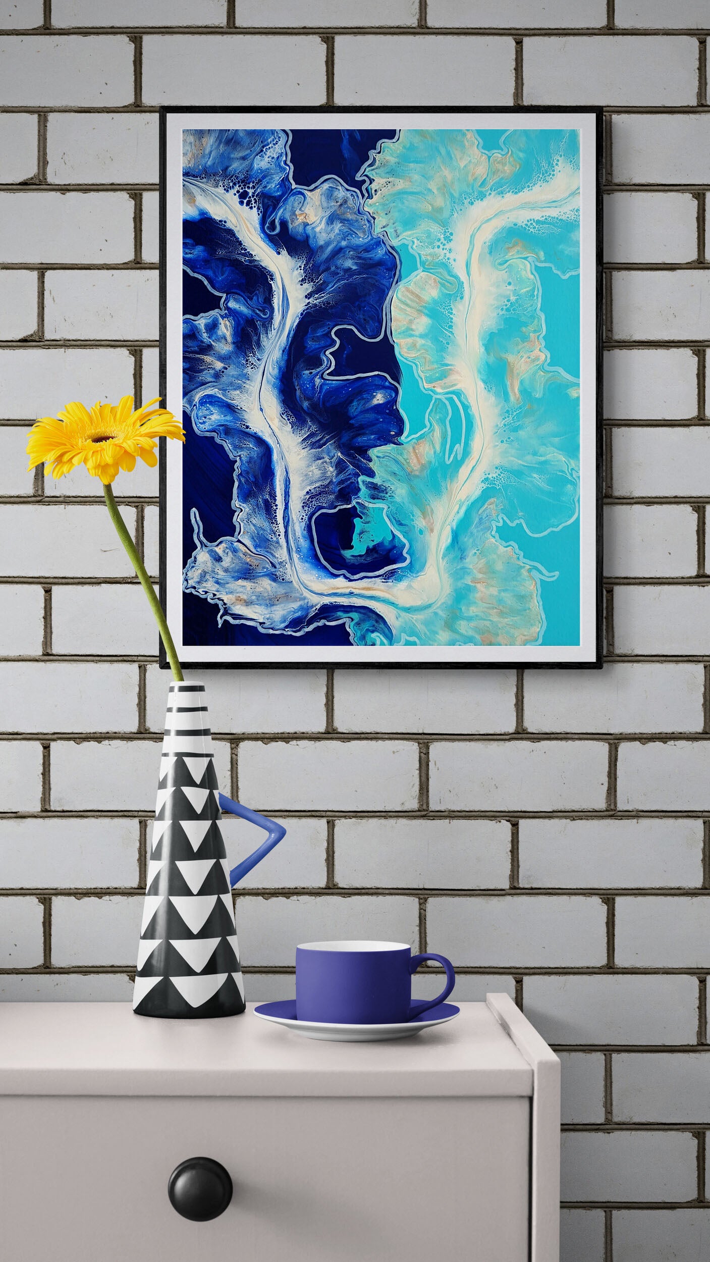 The Fine Line – abstract fluid art print in deep navy and aqua blue with ivory accents, framed wall art styled with yellow flower vase and blue cup.
