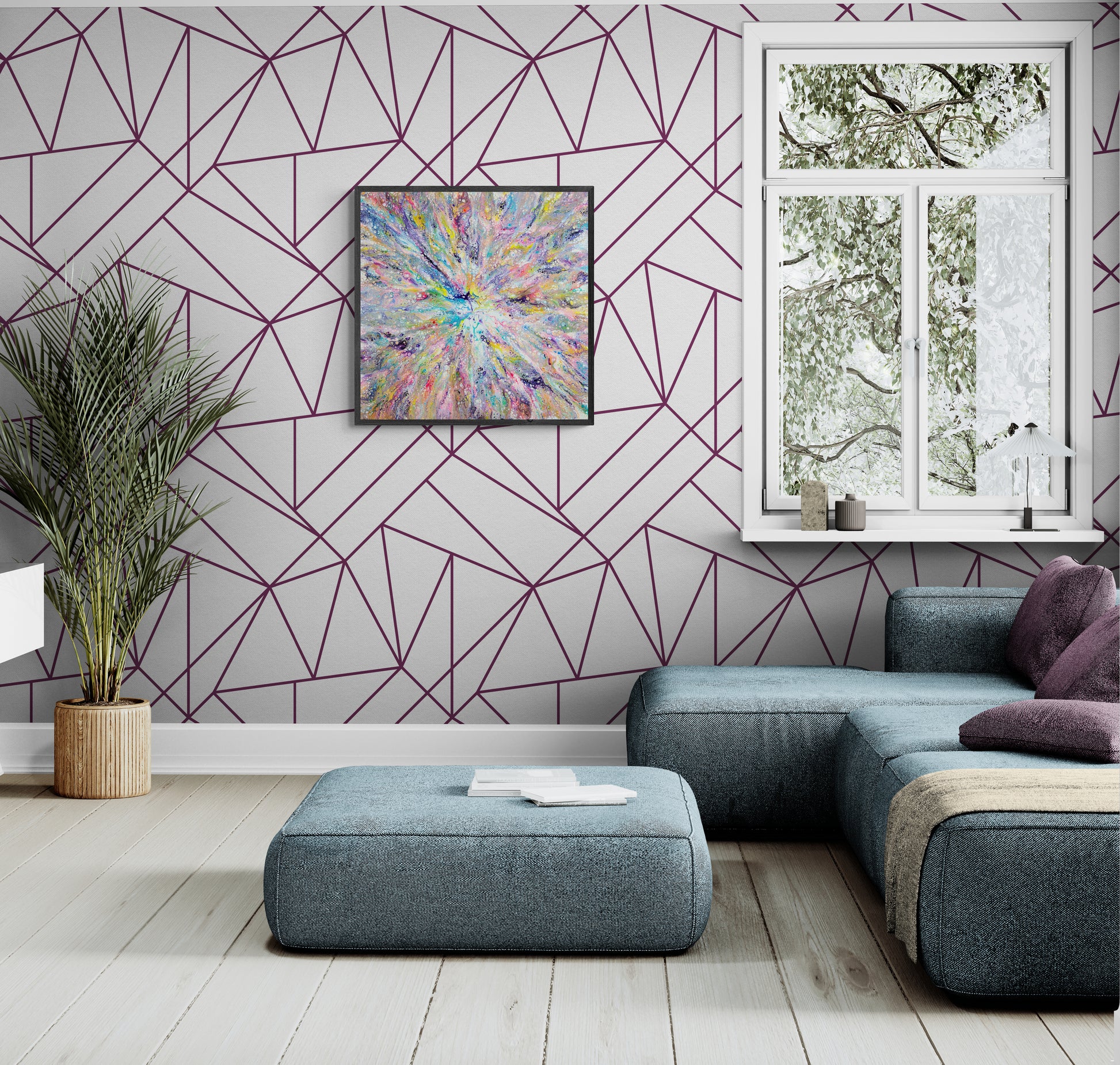A vibrant abstract fluid painting with a burst of rainbow colors radiates from the center and hangs on a light gray wall with geometric purple linework. The room features a modern blue sectional with purple pillows, a low ottoman, and soft wood flooring. A window lets in natural light, and a leafy plant in a wicker pot adds a natural element to the bright, contemporary space.