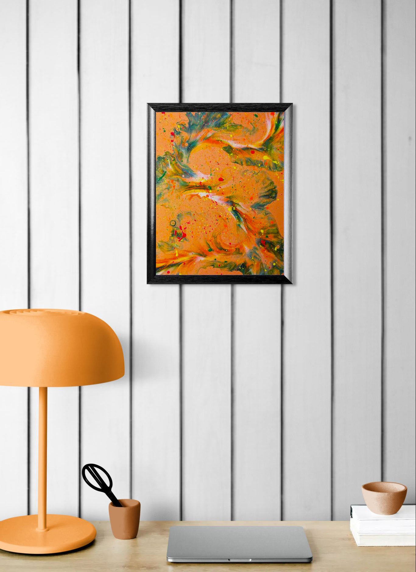 'Are You Really Going Out in That?' painting displayed on a light wood-paneled wall above a workspace, styled with an orange lamp, small desk accessories, and a laptop.