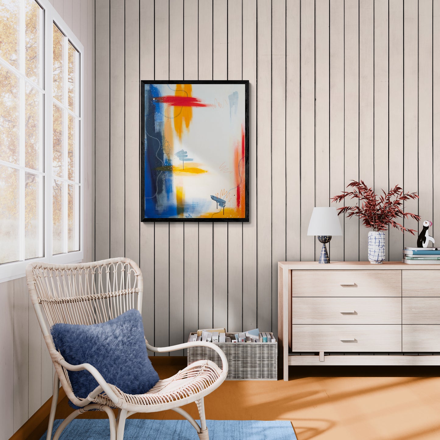 Framed abstract acrylic painting Be Bold by Abby May displayed in a neutral sitting area with a woven chair, blue cushion, and warm natural light
