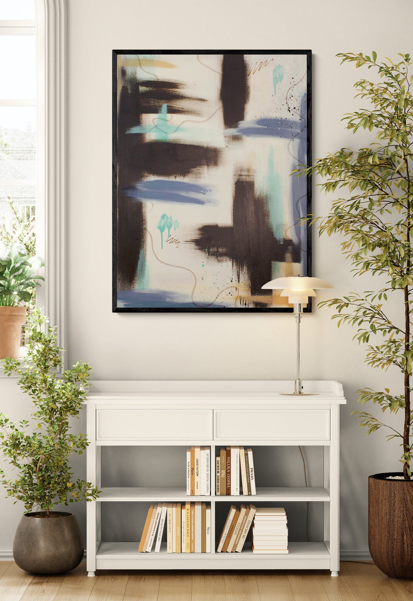 A vertical abstract art print in a black floater frame hanging on a cream wall. The artwork, "Between the Layers," features a mix of raw umber, teal, and soft purple-grey tones. It is styled above a white open-shelf unit filled with books and flanked by large indoor plants.