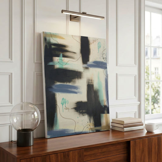 A canvas print of the painting sitting on a wooden side table. There's an overhead lamp, a globe lamp, and a stack of books and coffe cup near it.