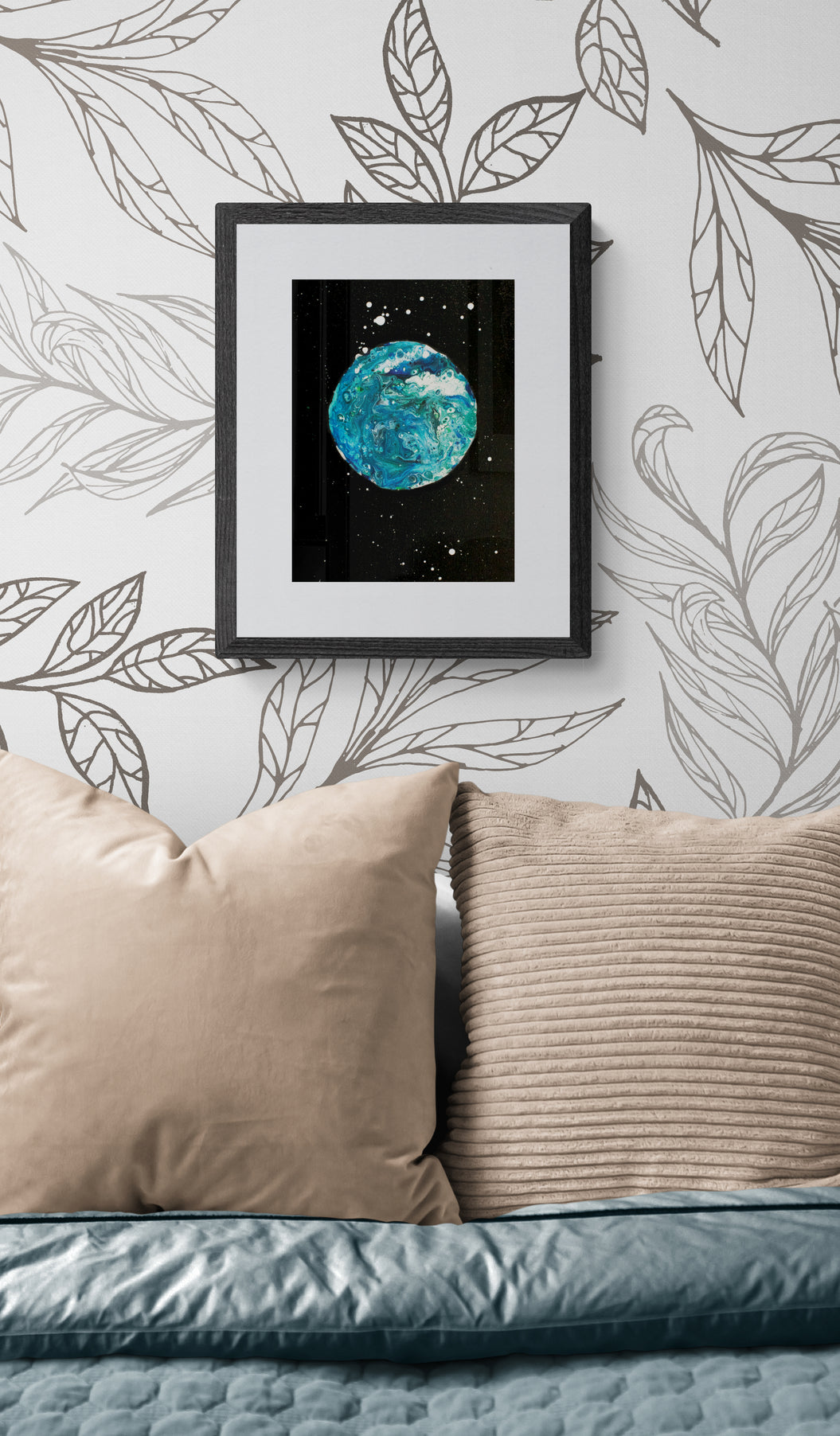 Blue Moon art print in a black frame displayed above a bed with soft blue and beige pillows, styled with modern leaf wallpaper