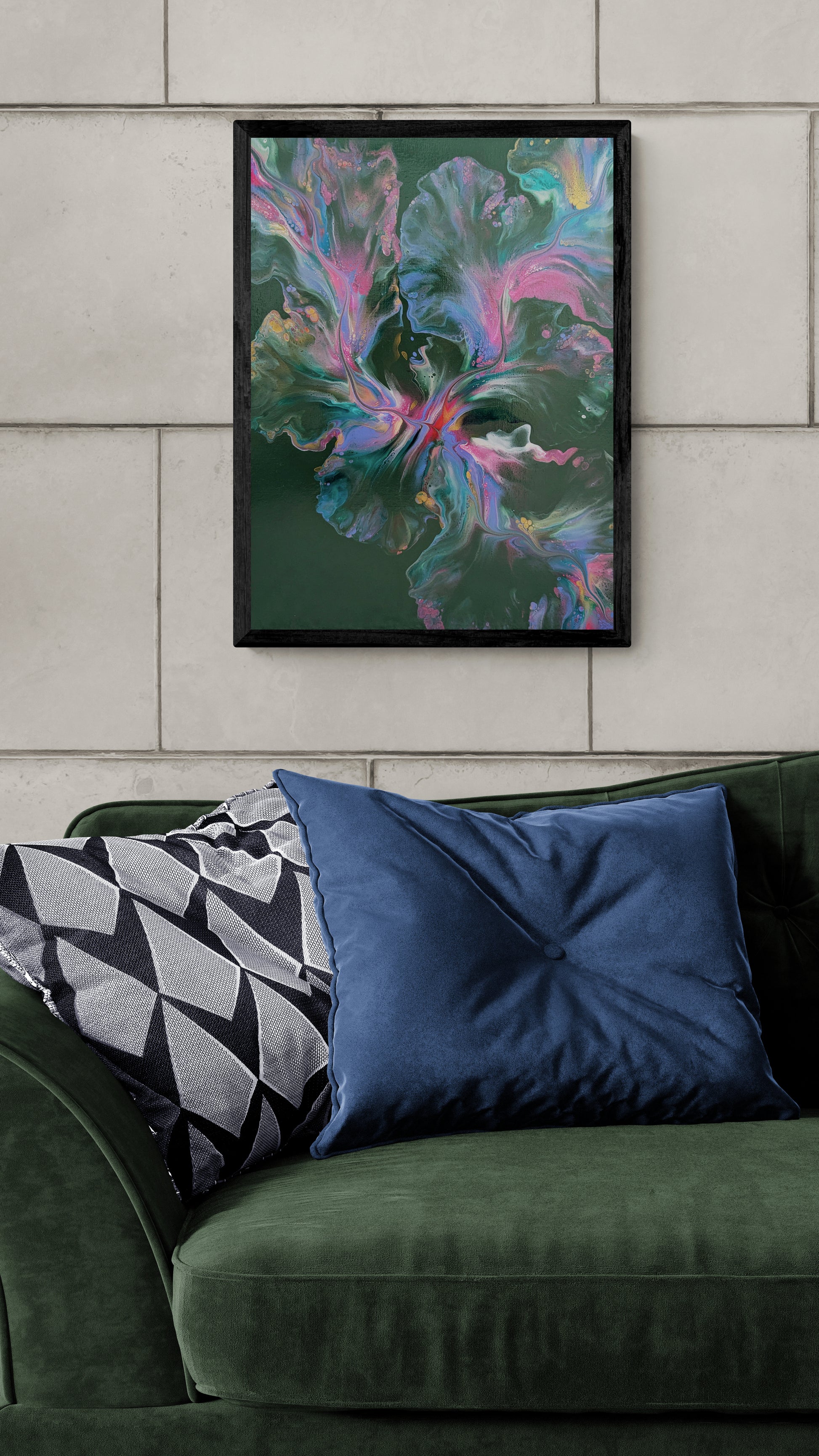 An abstract painting titled "Enchanted Sky" is framed in black and displayed on a stone tile wall. The artwork features dreamy swirls of pink, teal, lavender, gold, and soft white over a deep forest green background. Below, a plush green velvet couch is styled with a navy blue velvet pillow and a black-and-white geometric one, creating a rich, elegant, and visually layered living room scene.