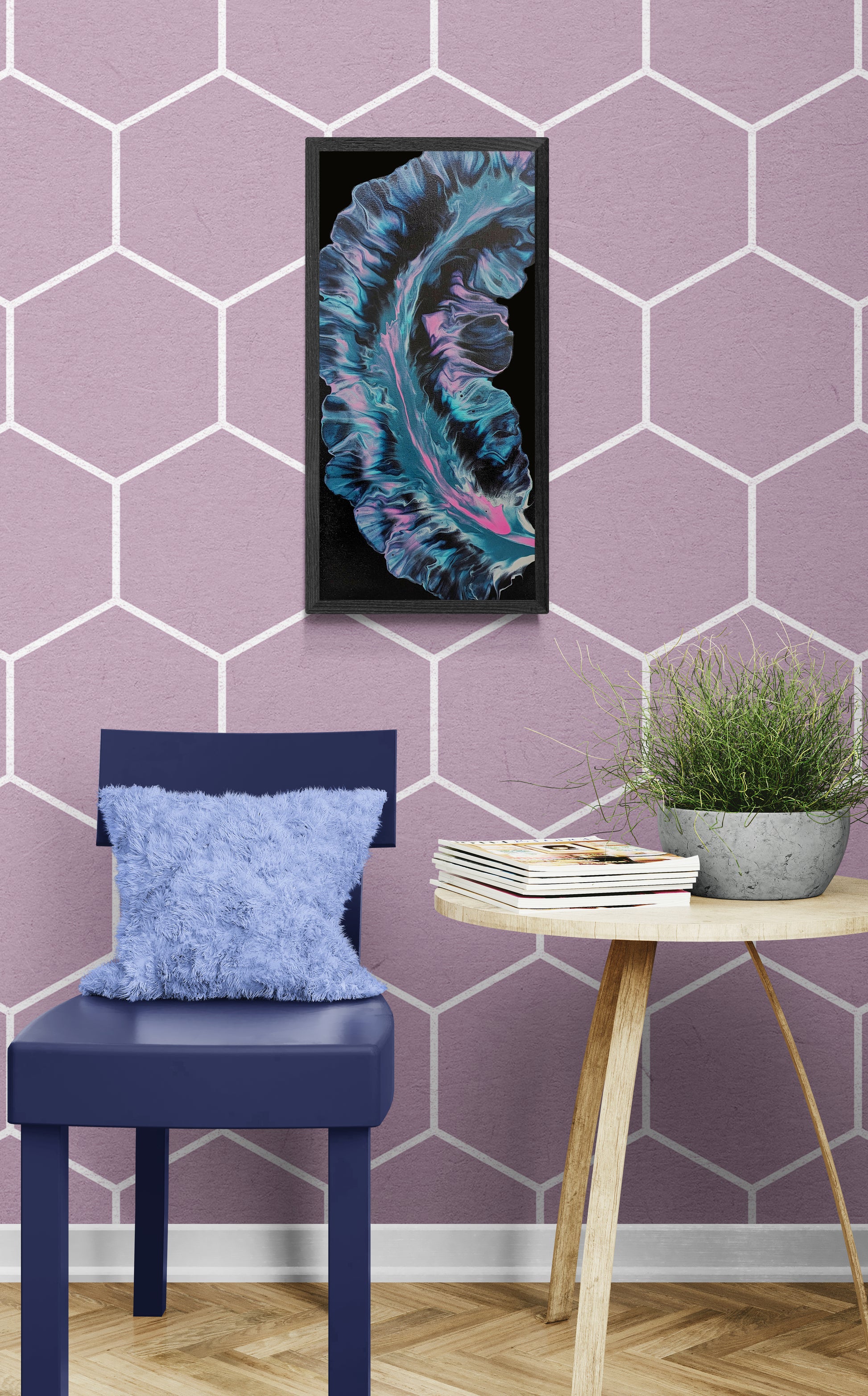 Framed abstract painting with flowing teal, violet, and pink tones on a black background, displayed on a pastel lavender geometric wall above a dark blue chair with a fuzzy pillow and a small round table holding books and a potted plant.