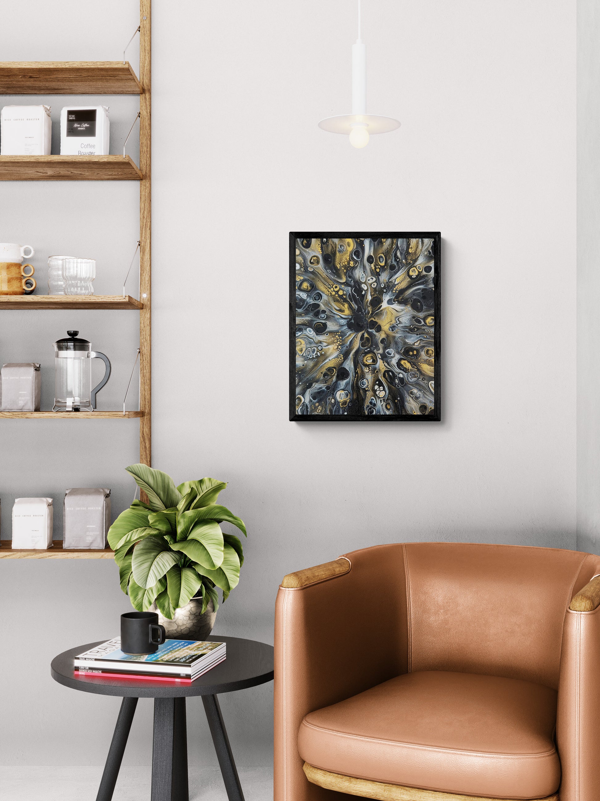 Abstract fluid art print in black, gold, and gray tones framed in black, hanging above a tan leather chair beside a small round table with a plant and coffee mug.