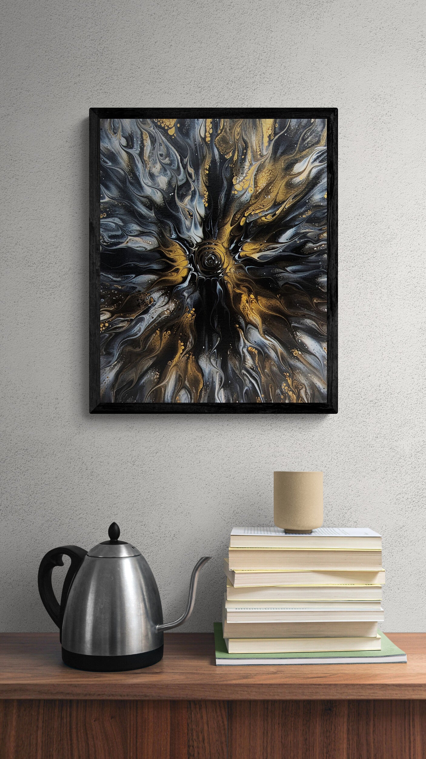 Black-framed abstract fluid art print with swirling gold and gray tones displayed above a wooden shelf with a stack of books and a stainless steel kettle