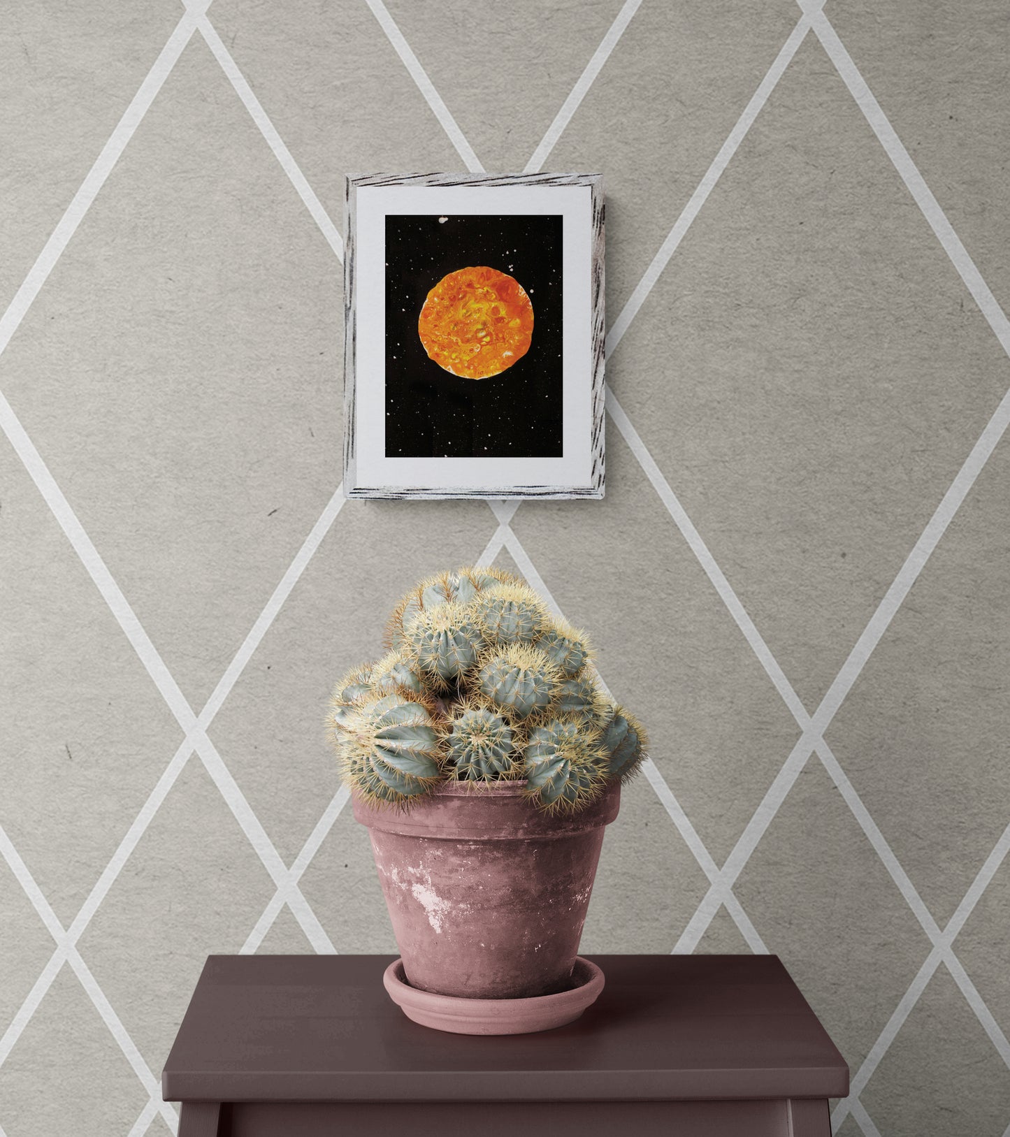 Harvest Moon art print in a rustic white frame on a diamond-patterned wall with a cactus plant below