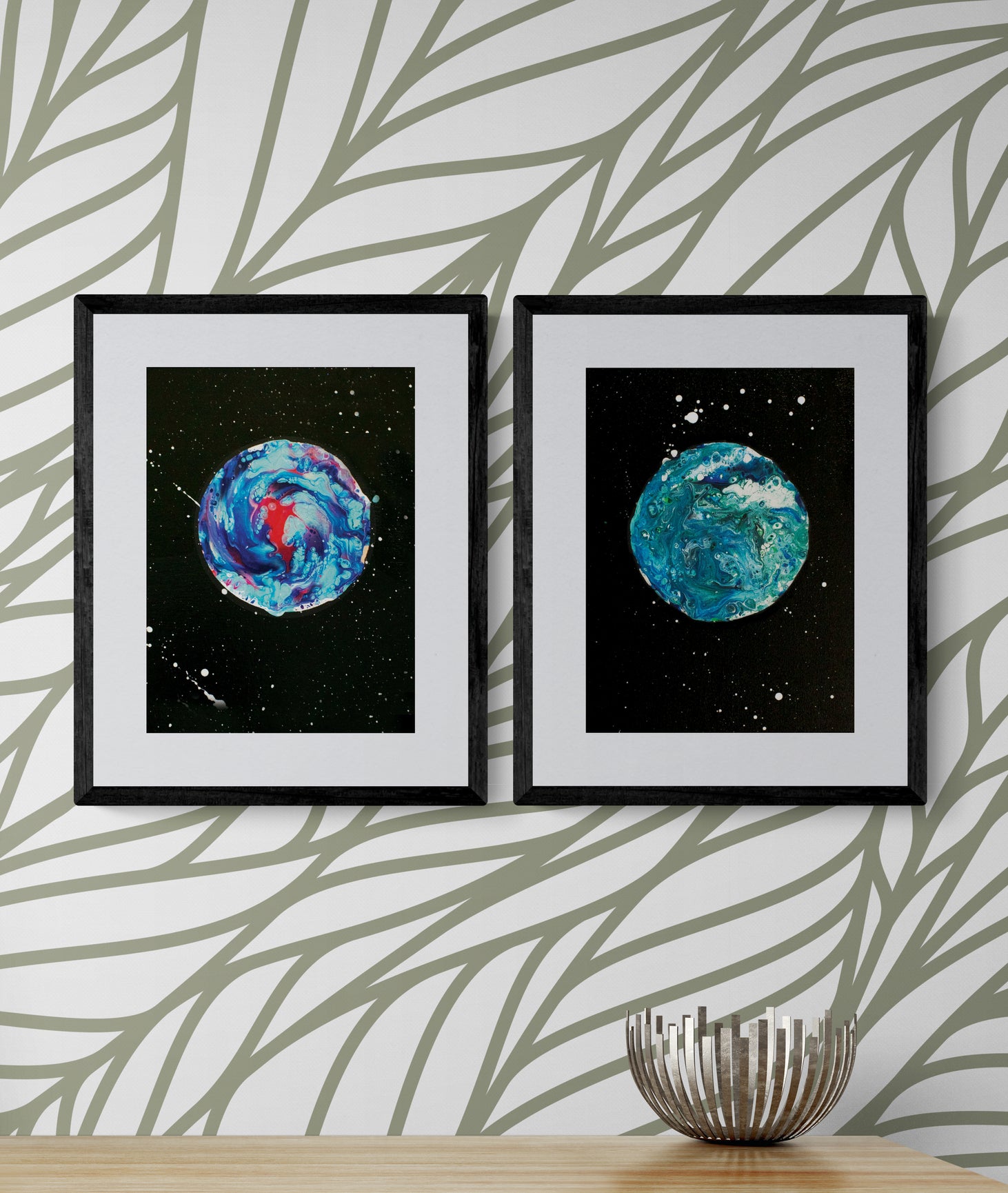 Her Majesty The Moon and Blue Moon framed prints hung on a wallpapered wall with abstract sage green leaf patterns and a silver bowl on the wood console below.