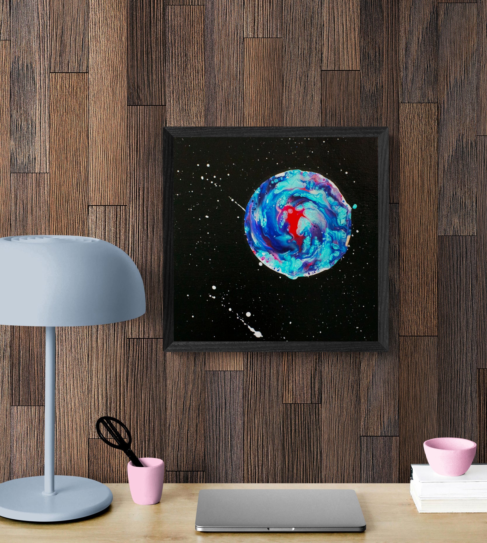 Close-up view of Her Majesty the Moon framed painting on a wood-paneled wall above a workspace with lamp and laptop.