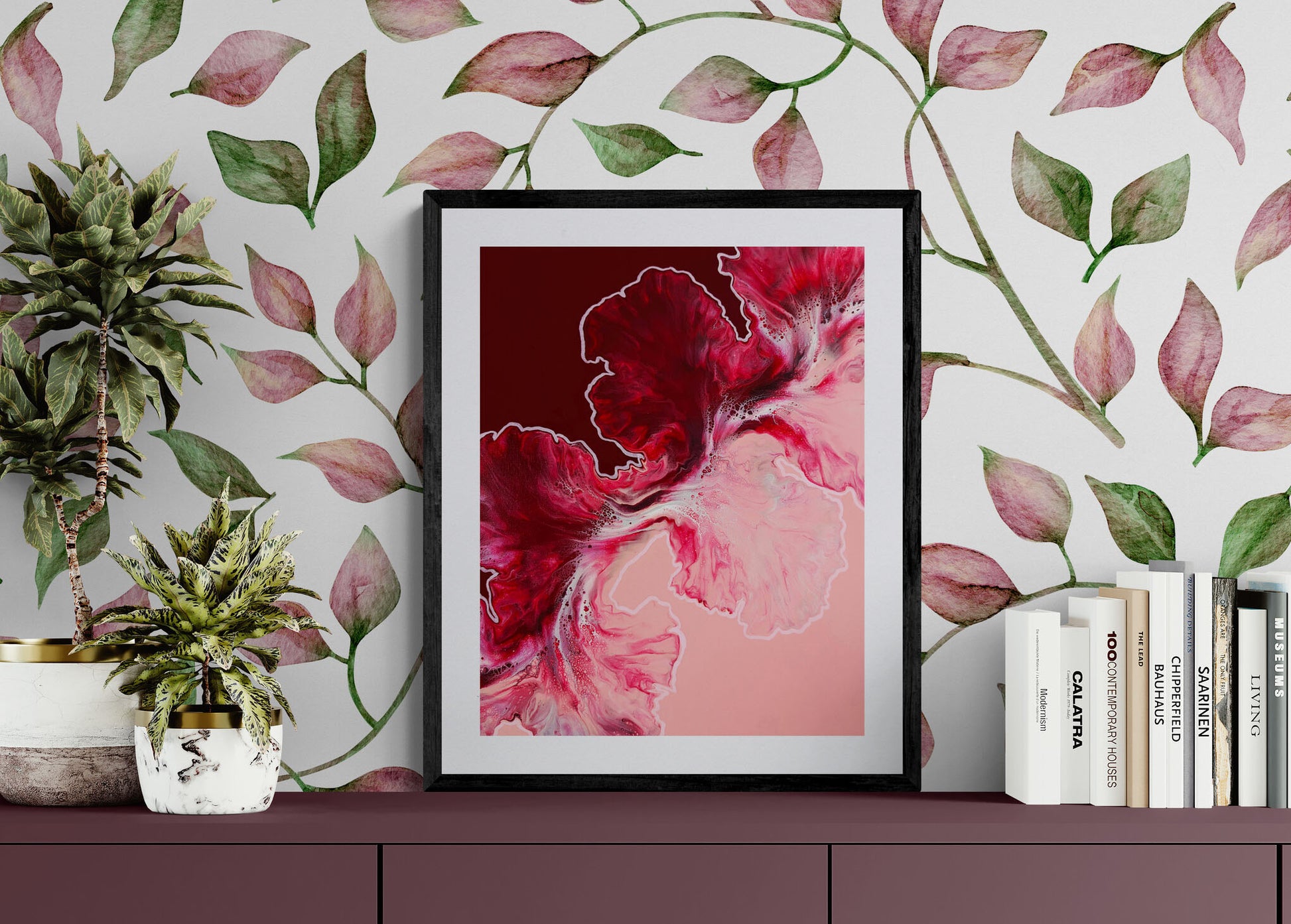 Abstract fluid art print in rich burgundy, crimson, and blush pink tones, framed on wall with floral wallpaper.