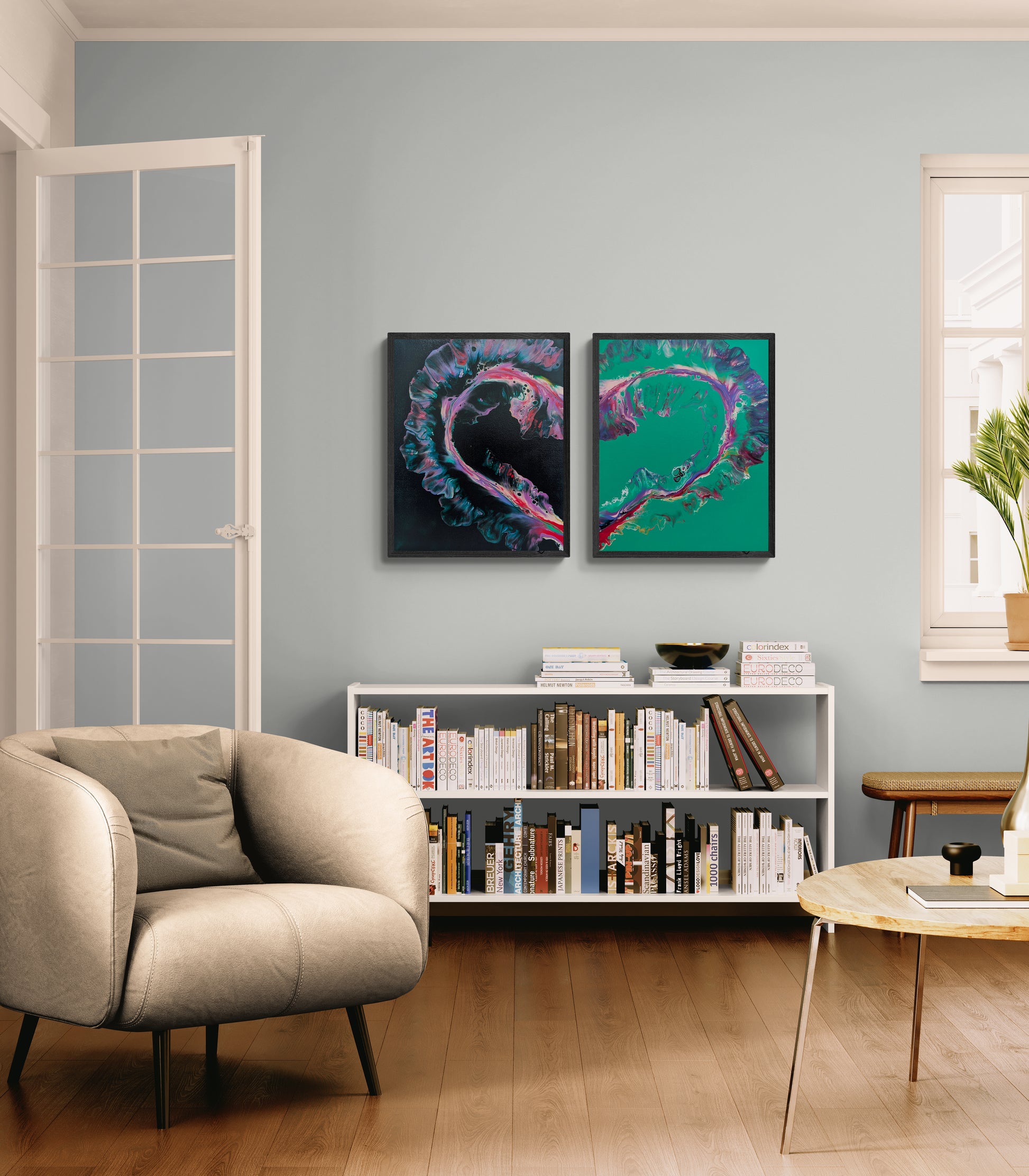 Two abstract heart-shaped fluid paintings are displayed side by side above a white bookcase in a modern living room. One canvas has a black background with vivid pink, teal, and purple accents. The other features a green background with matching flowing colors. Together, the canvases form a single heart shape, creating a bold, emotional centerpiece in the softly lit space.