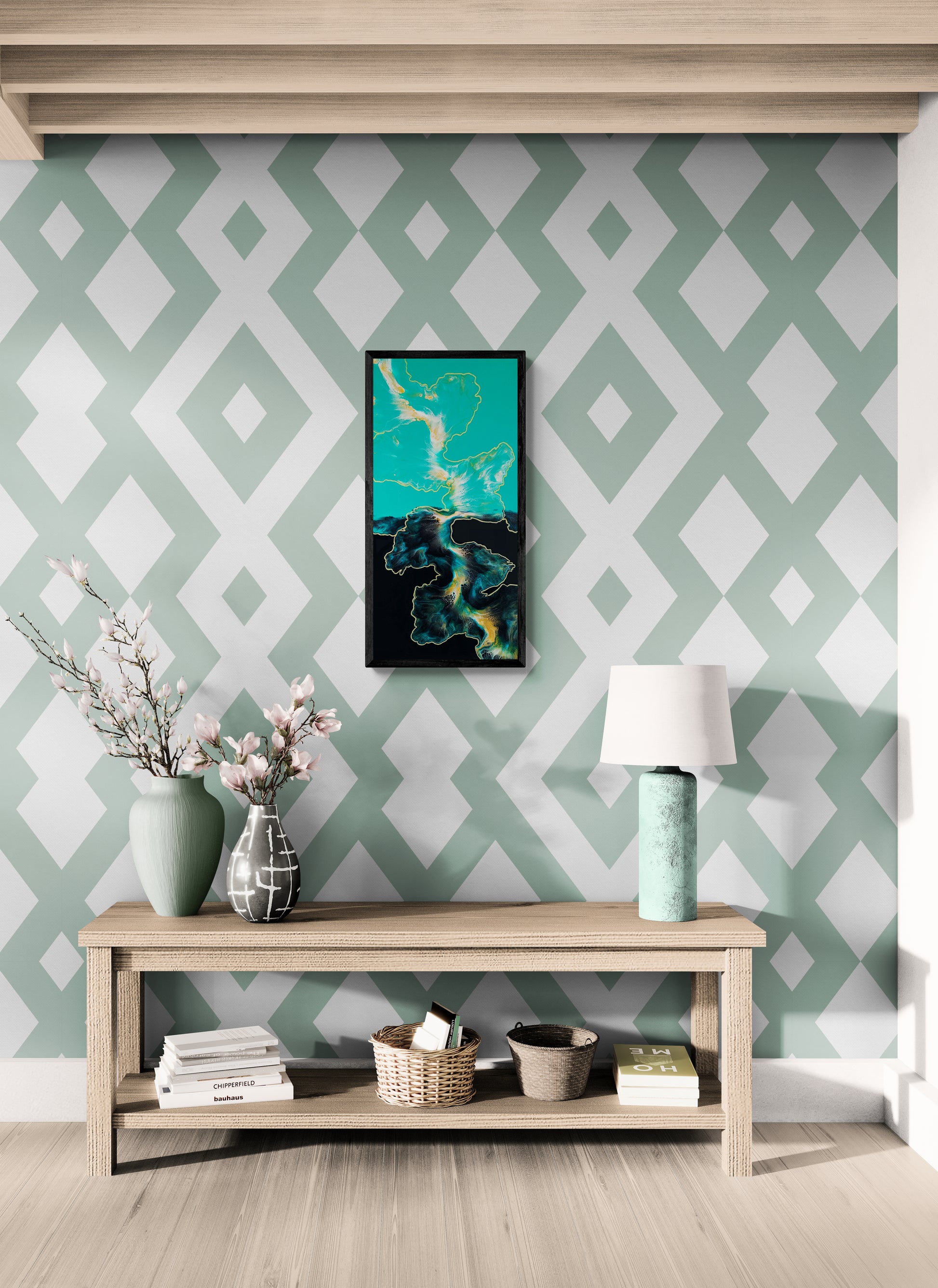 A bold abstract painting titled "Outside the Lines" is framed in black and displayed on a patterned green-and-white geometric accent wall. The artwork features flowing shapes in teal, white, black, and gold, evoking maps or tide lines in motion. Below the painting sits a natural wood bench styled with vases of pink blossoms, a seafoam lamp, books, and woven baskets, creating a modern and welcoming entryway scene.