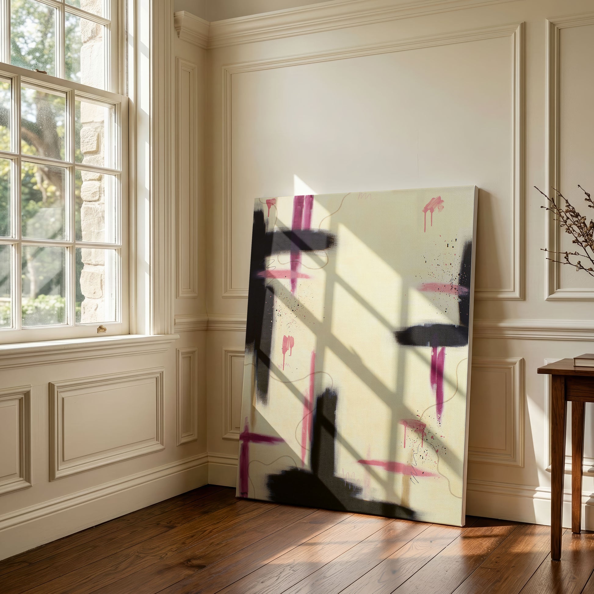 Lifestyle view of the large abstract canvas print leaning against a white wall on a wooden floor, styled next to a small side table and a bright, paned window.