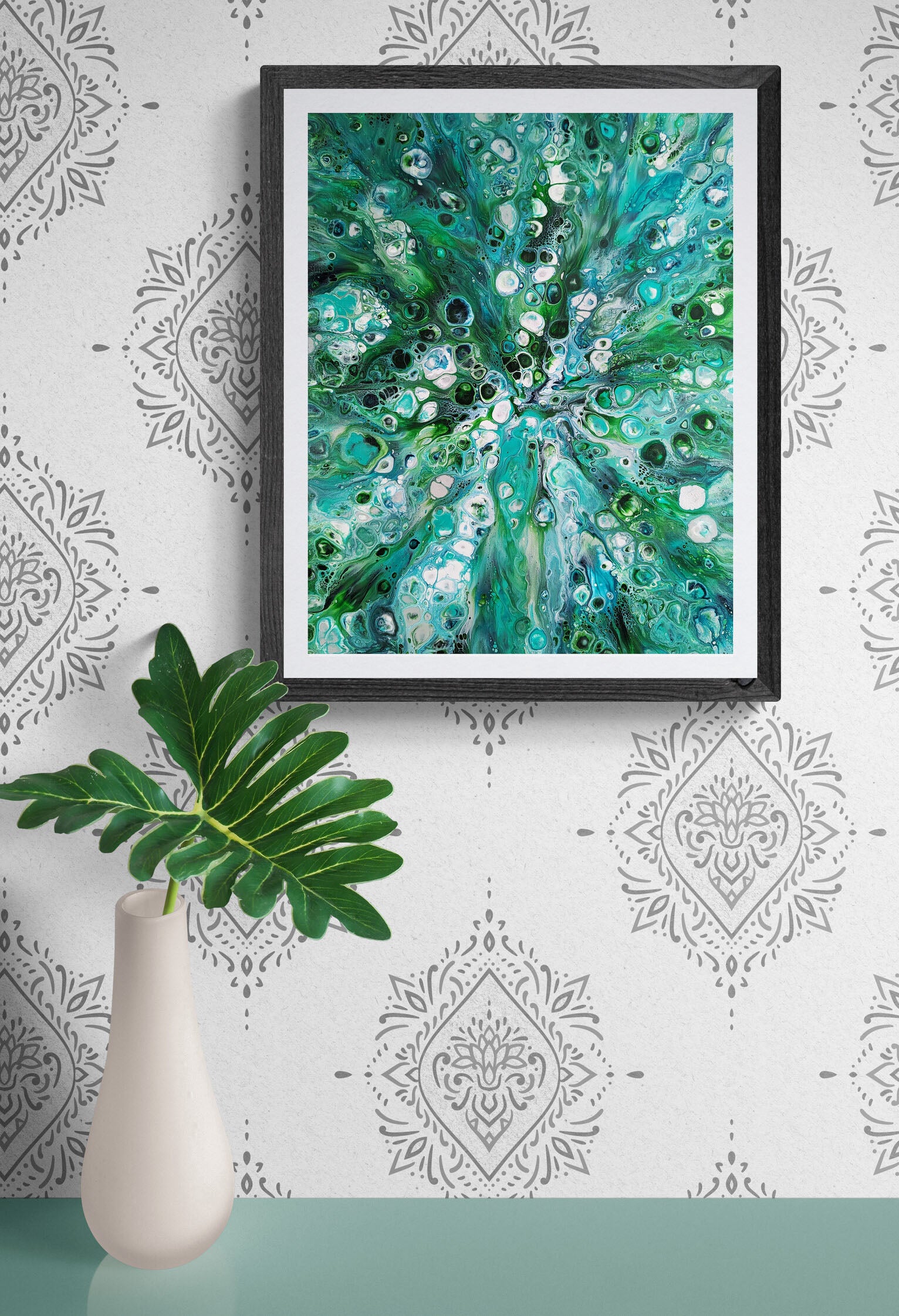 Abstract fluid painting print Sea Maiden framed and styled above a minimalist vase with a tropical leaf, design showcasing oceanic blues and greens with flowing organic shapes.