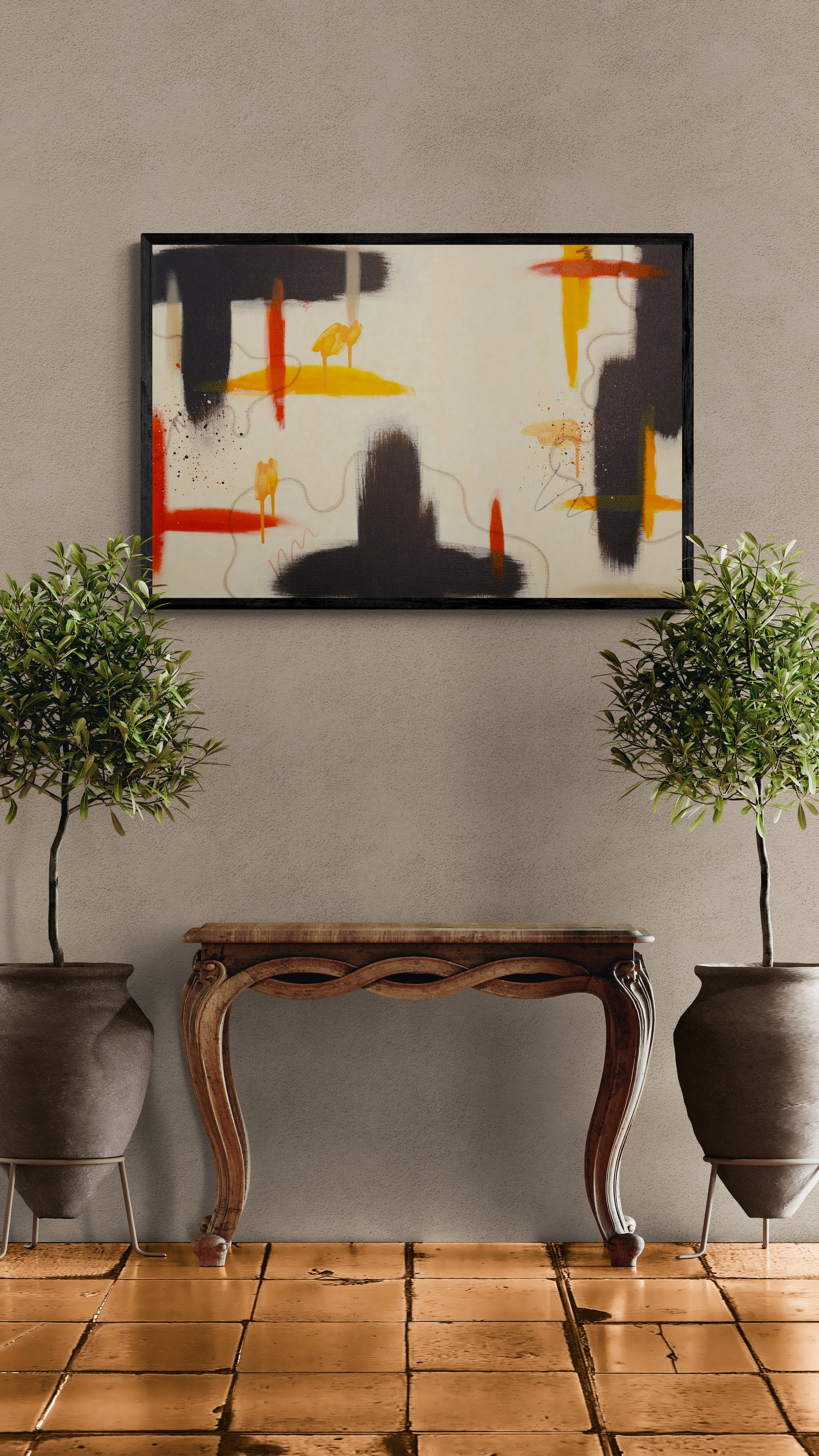 A framed horizontal abstract painting with raw umber, yellow, and red accents displayed in a black floater frame. The artwork is centered on a textured beige wall above an ornate wooden console table flanked by two large potted olive trees on a terracotta tiled floor.