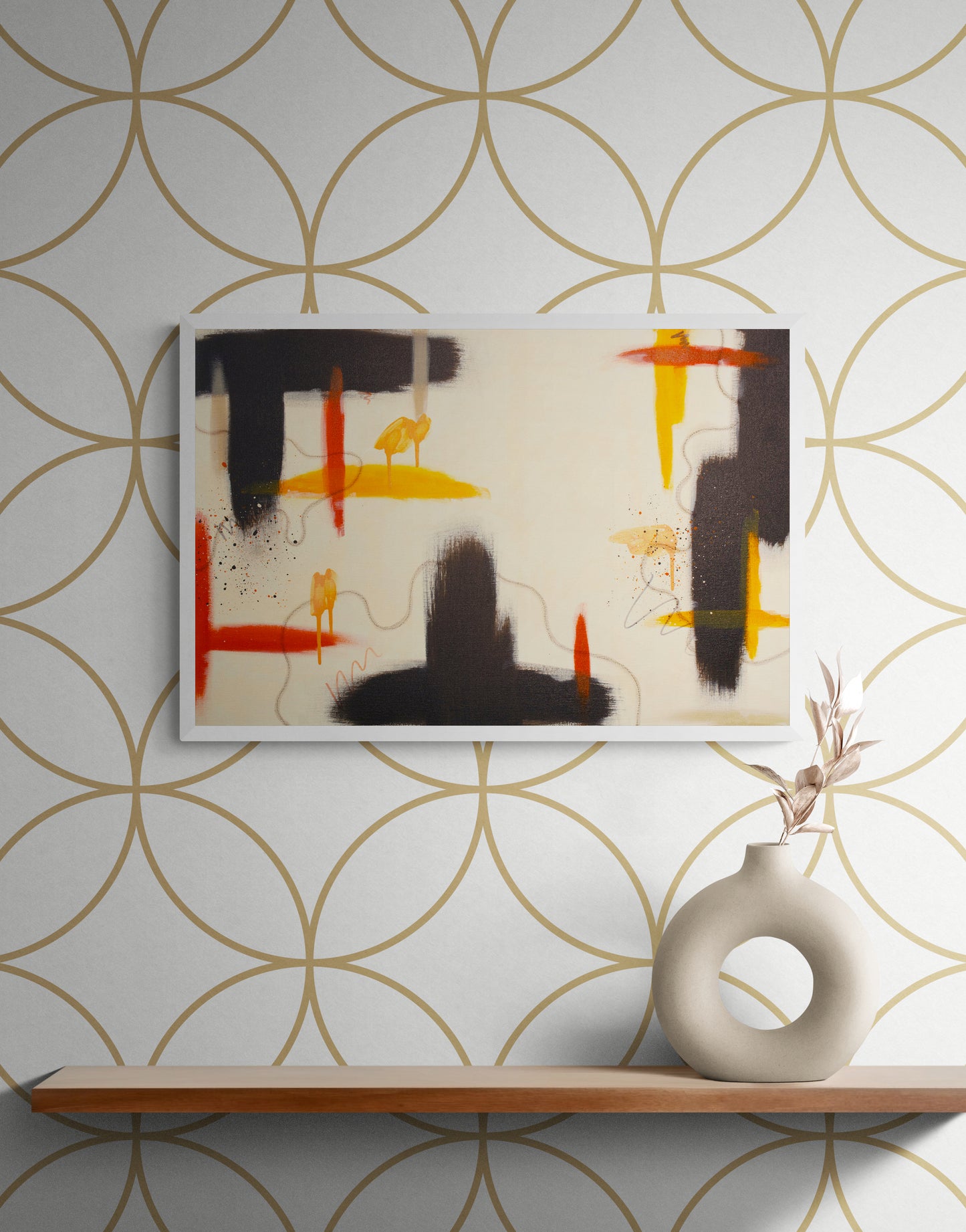 An abstract art print with deep raw umber shapes and yellow highlights mounted on a wall with a gold geometric circle pattern. Below the art, a light wood floating shelf holds a modern circular ceramic vase with a dried botanical branch.