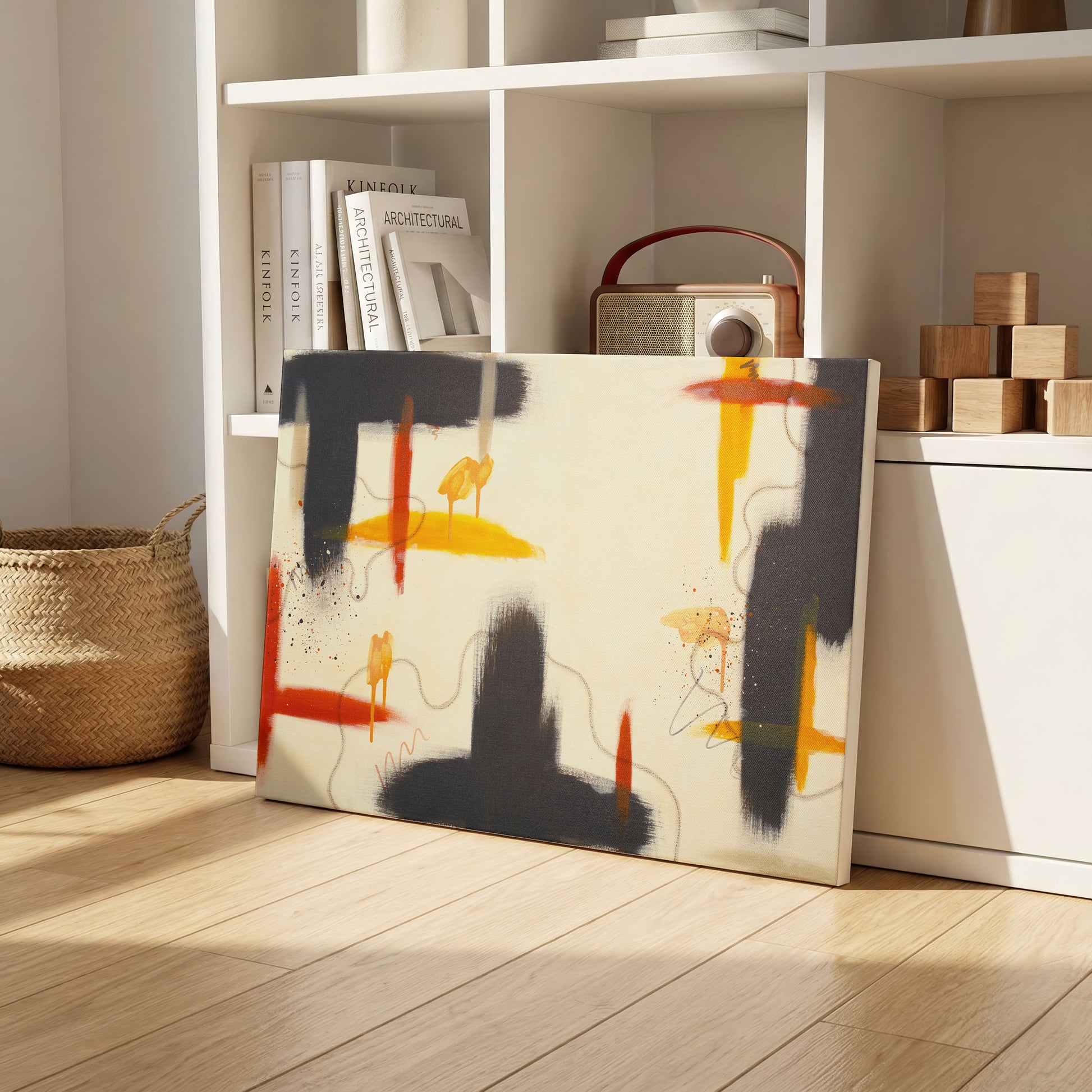 A canvas print of the painting leaning against a white shelf, sitting on a light wooden floor. On the shelves are books, wooden blocks, and old school radio, and a weaved basket on the left.