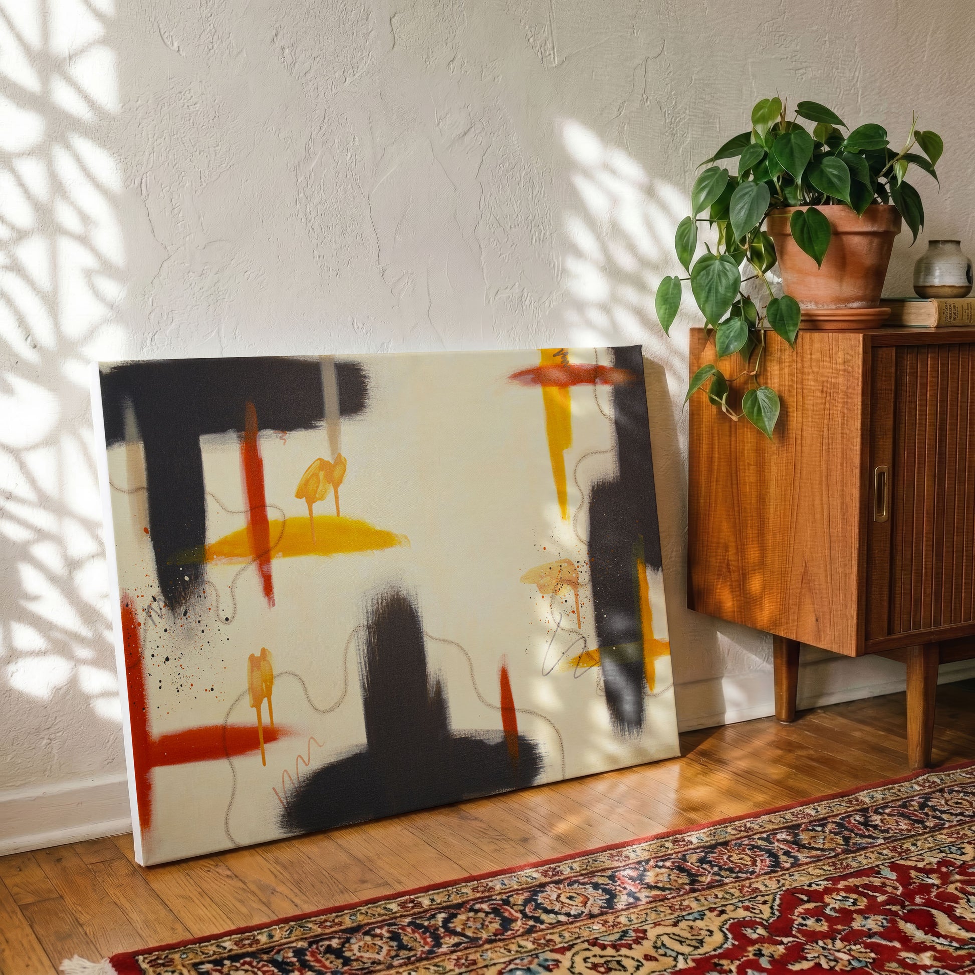 A canvas print of the painting leaning against a textured white wall, sitting on a wooden floor in front of a red patterend rug. A potted house plant on an armoire is on the right side of the print.