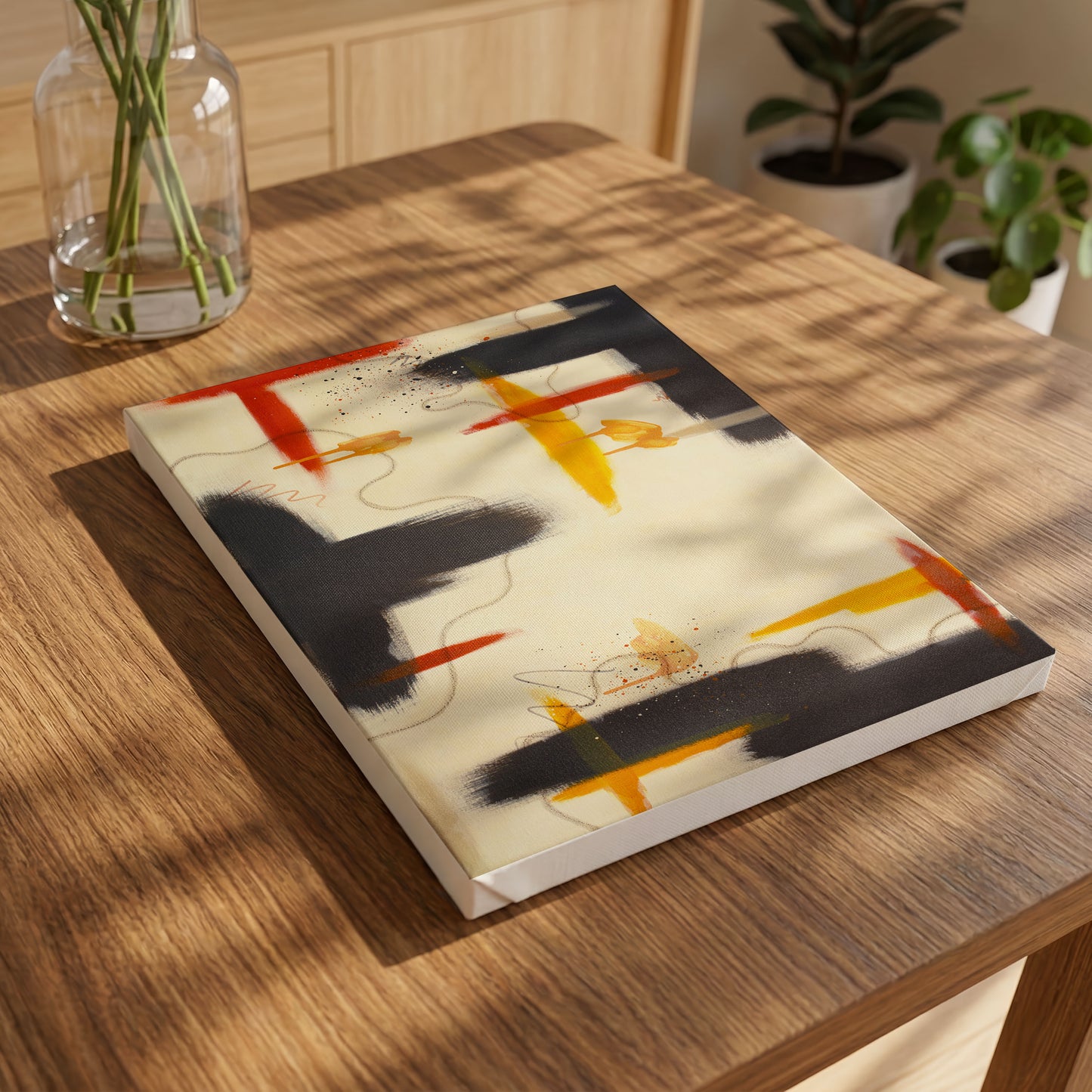 A small canvas print of the painting laying on a wooden table, with a glass vase in the top left. In the background to the left are two potted plants.