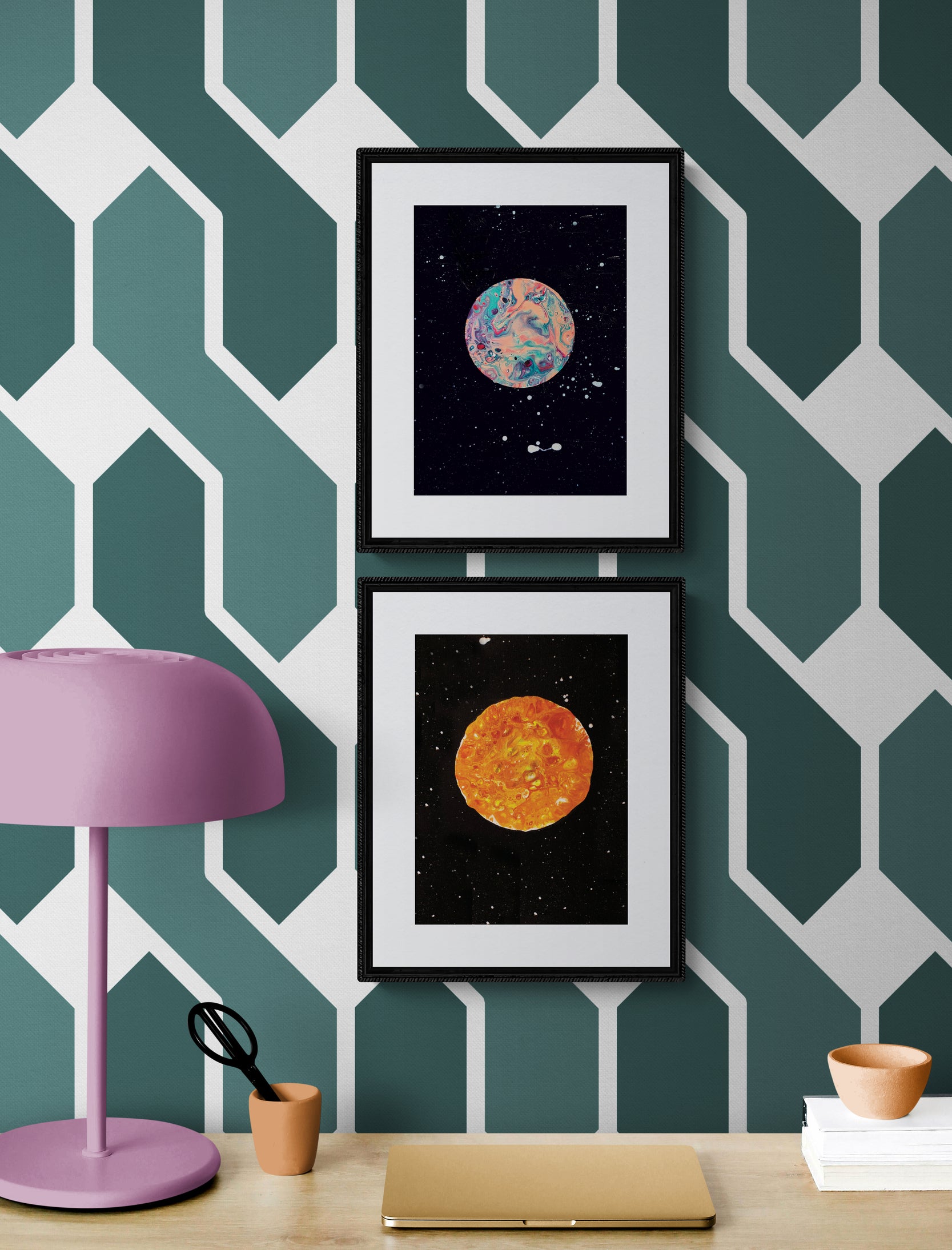 Strawberry Moon and Harvest Moon framed prints displayed vertically on a green-and-white herringbone wallpapered wall with a pink desk lamp and accessories.