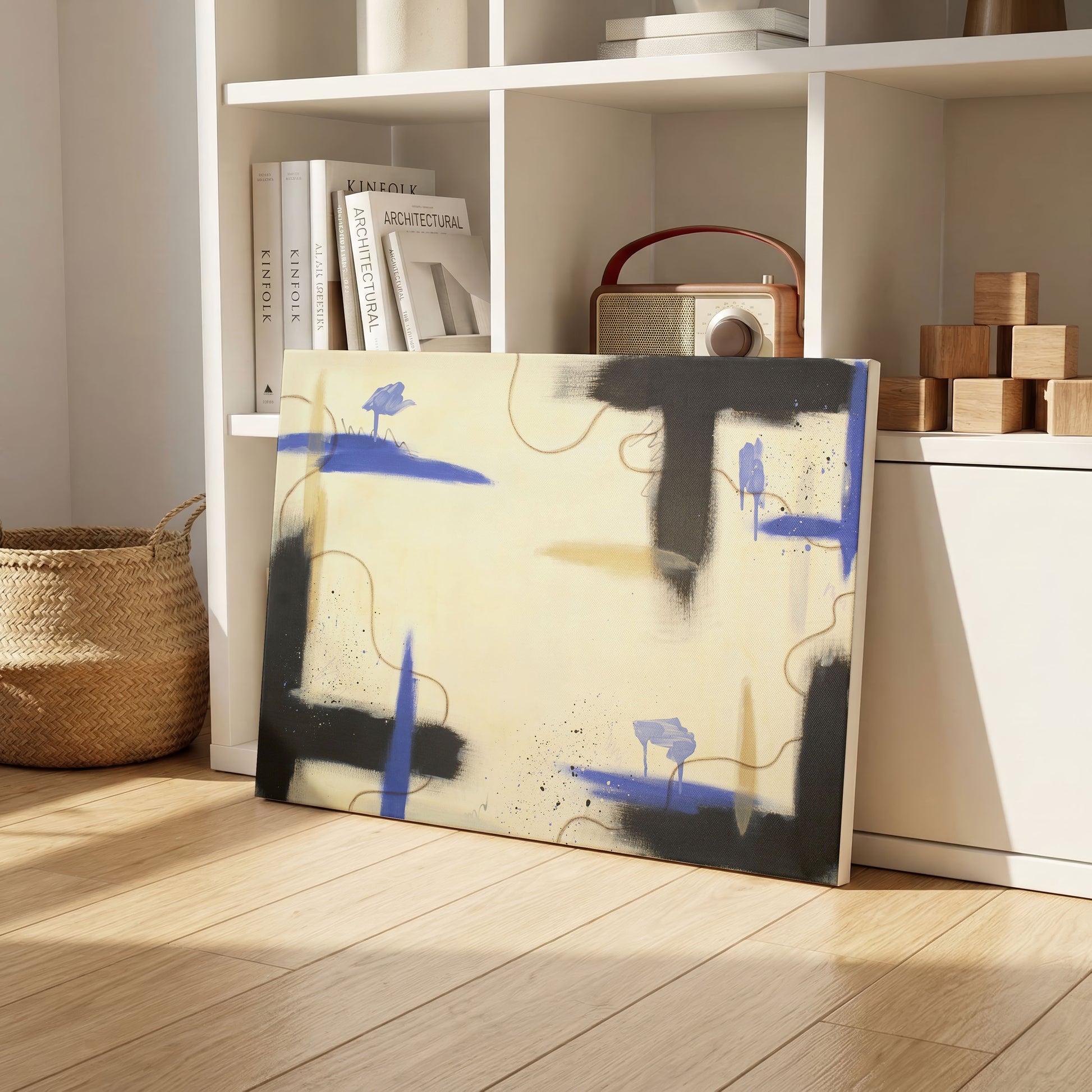 A canvas print of the painting sitting on a wooden floor, leaning against white, cubed shelving. The shelving spaces have wooden blocks, an old style radio, books, and various decorative pots. On the left is a brown, woven basket.